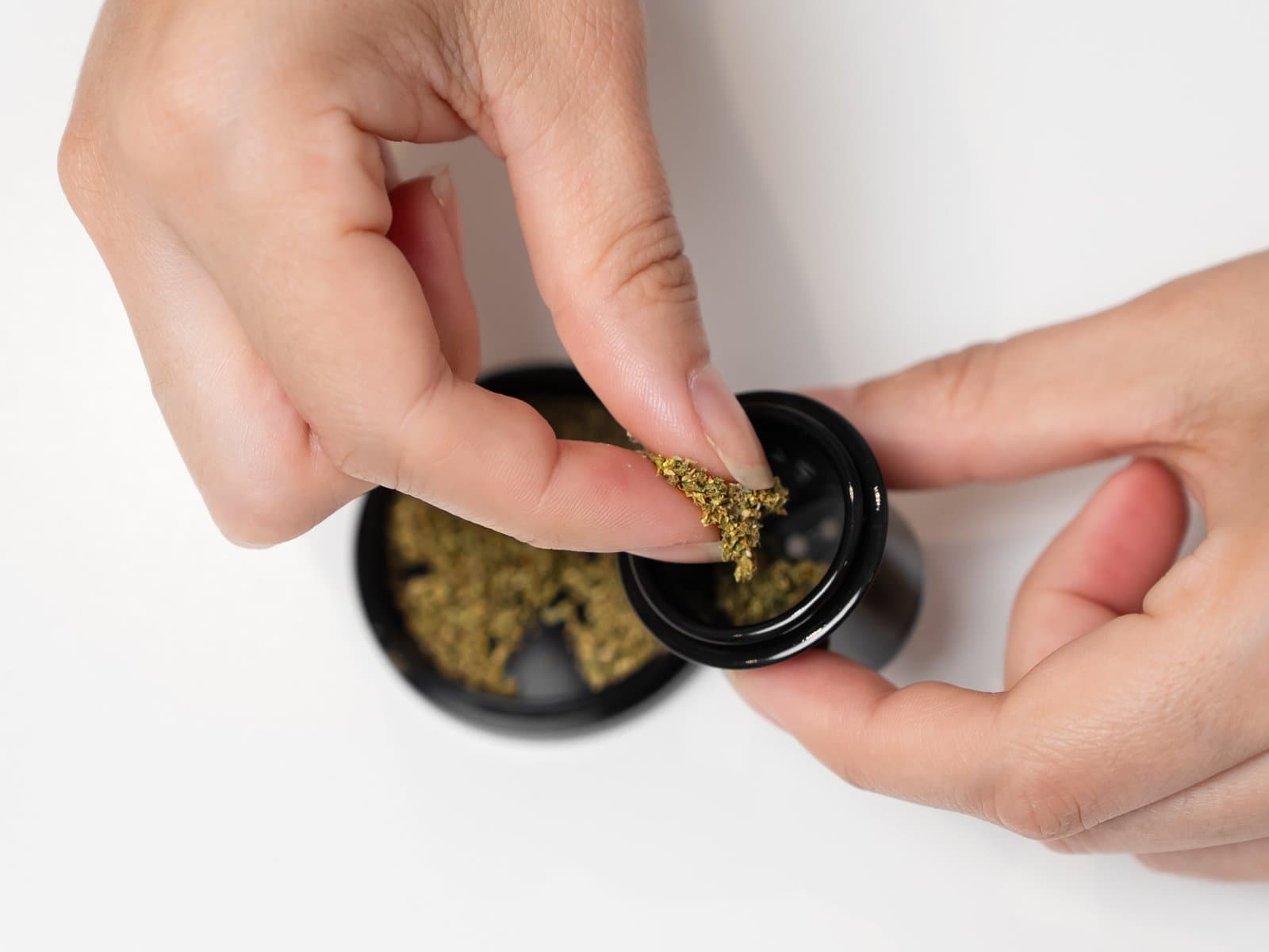 Hands packing ground cannabis into an AirVape Enso ceramic cup over an open grinder