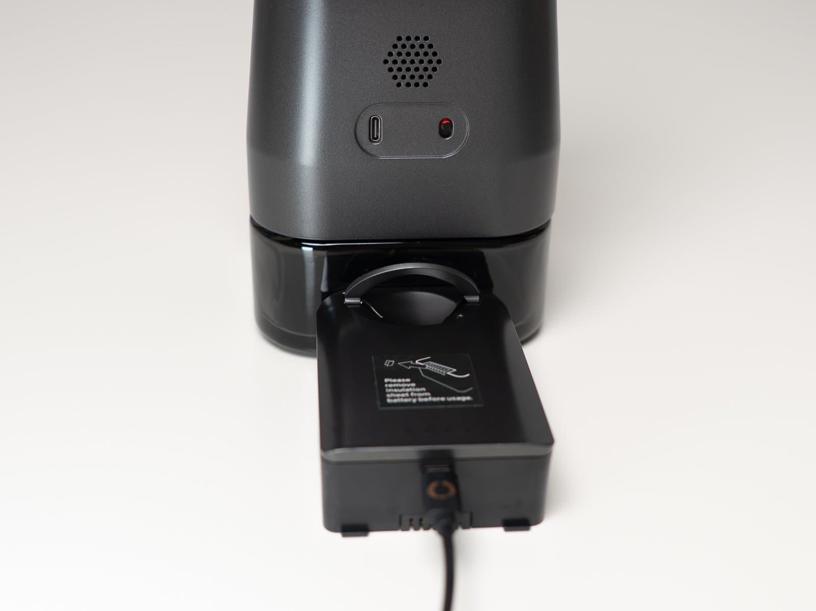 Herausnehmbarer 5000-mAh-Akkupack des AirVape Enso, abgenommen und per USB-C ladend vor dem Gehäuse, die leere Aufnahme zeigt ihren eigenen Anschluss und das Lautsprechergitter