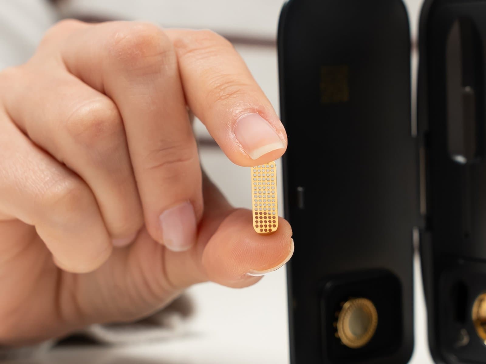 Fingers holding gold magnetic screen showing its small size near open device
