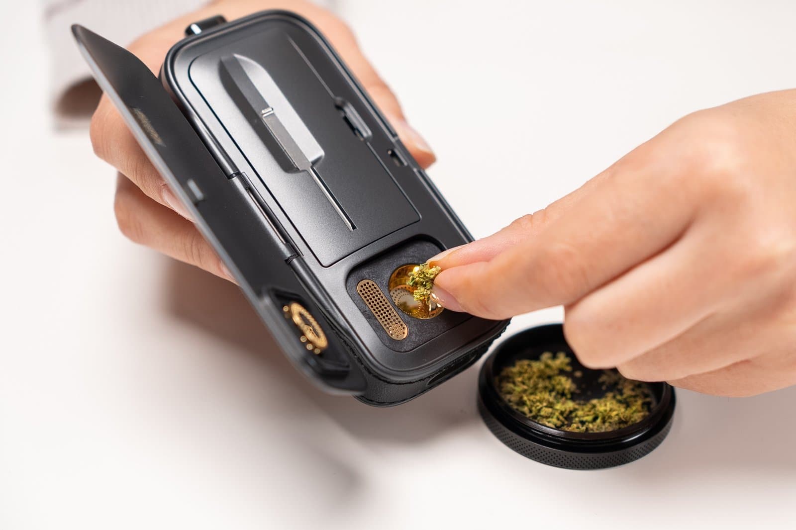 Loading ground cannabis into the gold-plated chamber of the AirVape Legacy Pro 2, with an open grinder below