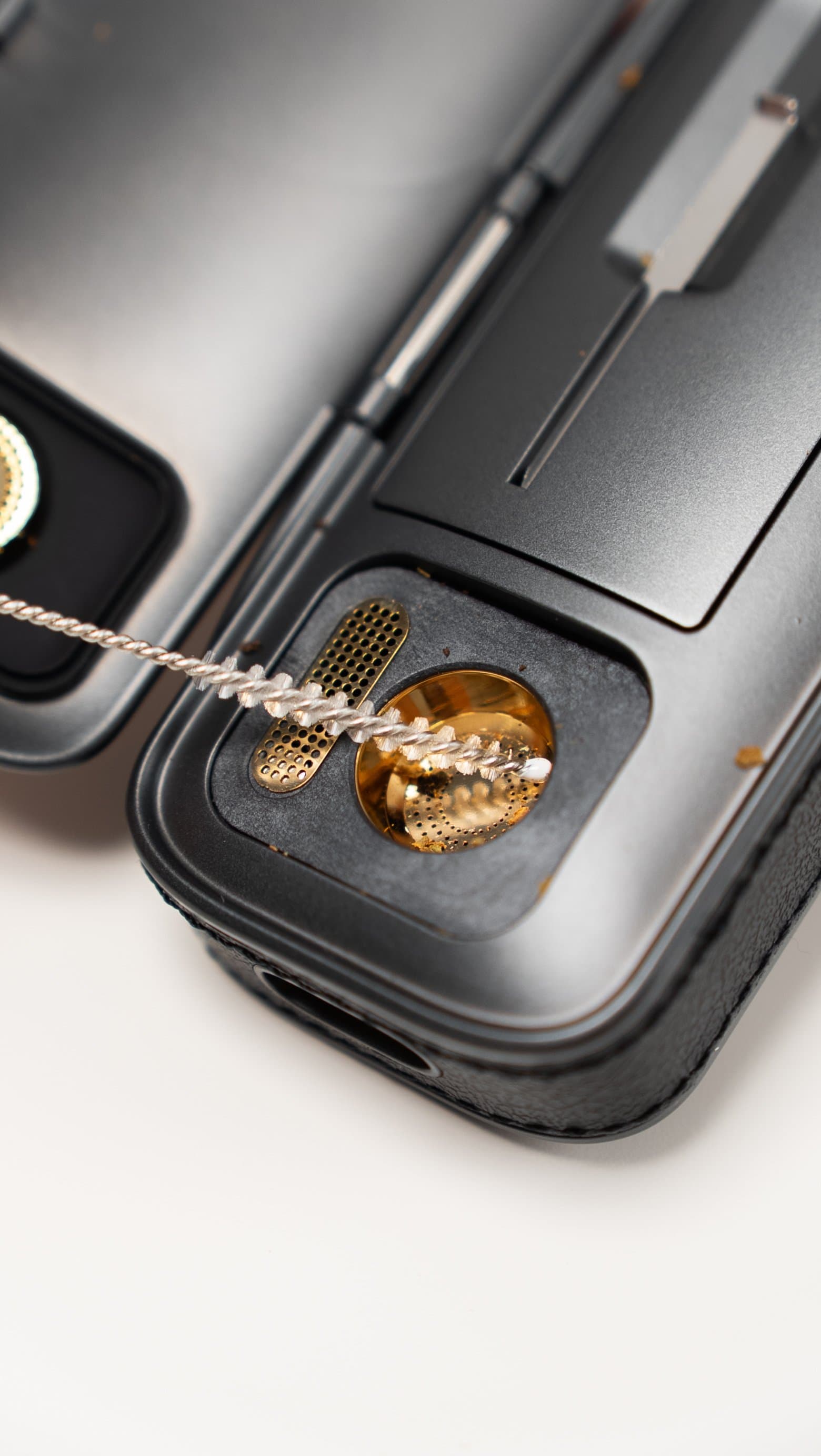 Brushing out the gold-plated chamber of the AirVape Legacy Pro 2 beside its magnetic screen