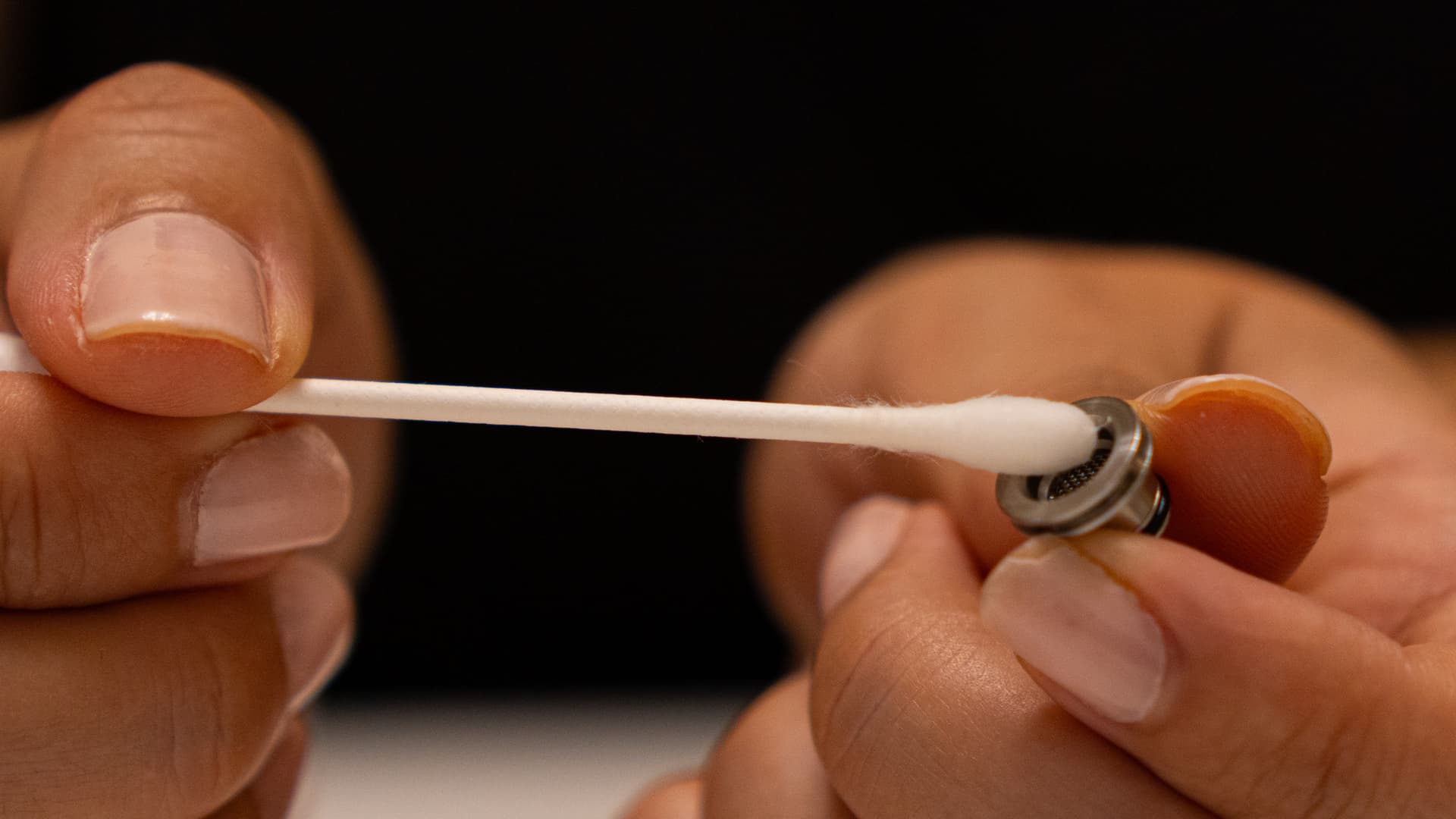 Close-up of hands using a cotton swab to clean a small stainless steel screen showing residue buildup