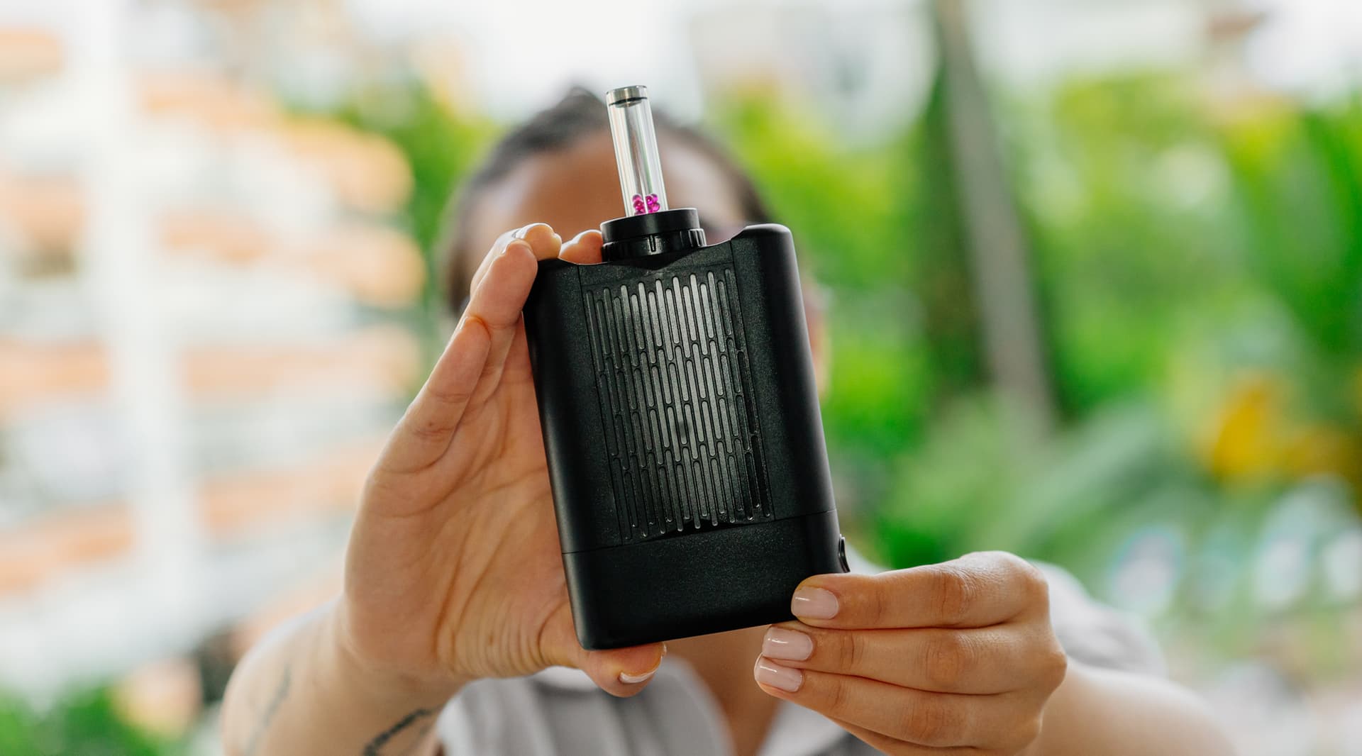 Angus Enhanced vaporizer held in hand outdoors with green foliage background