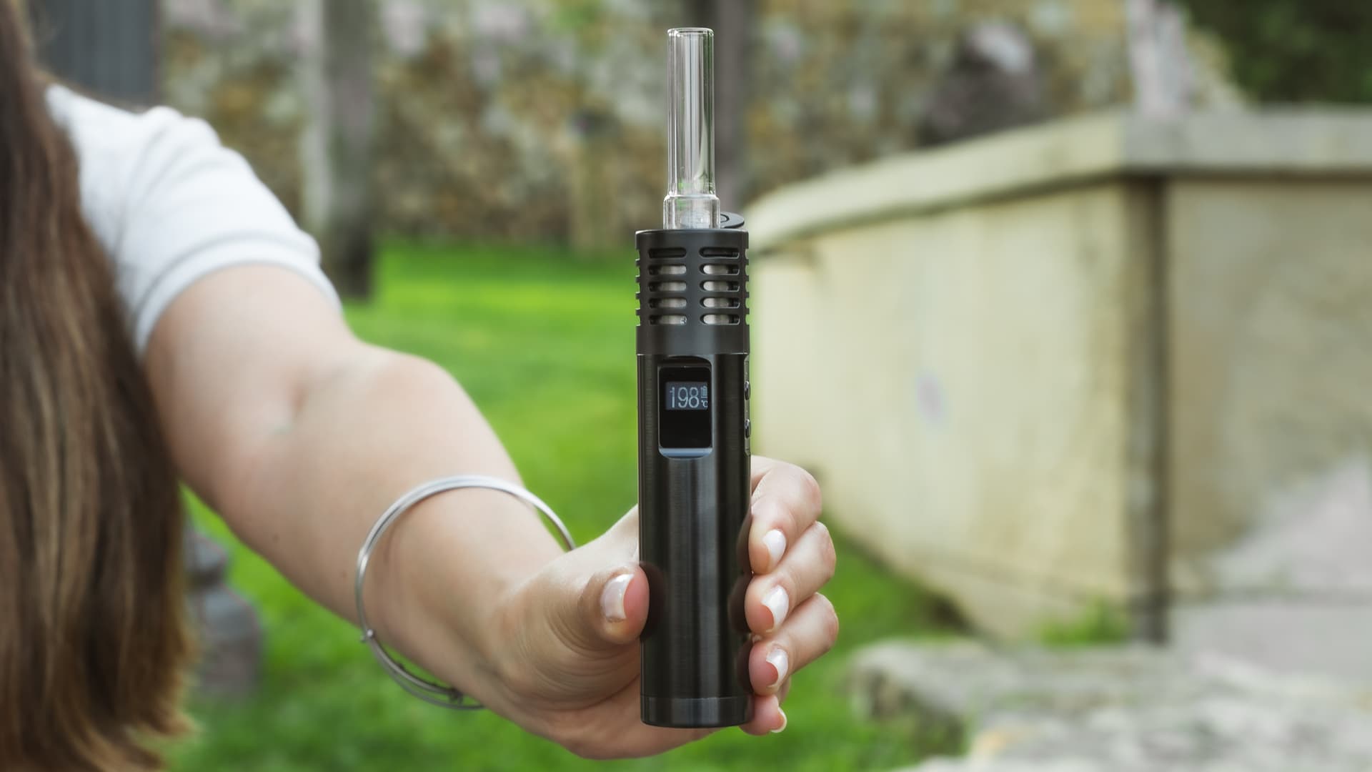 Arizer Air Max held outdoors showing 198°C on OLED display with glass stem inserted in anodized aluminum body