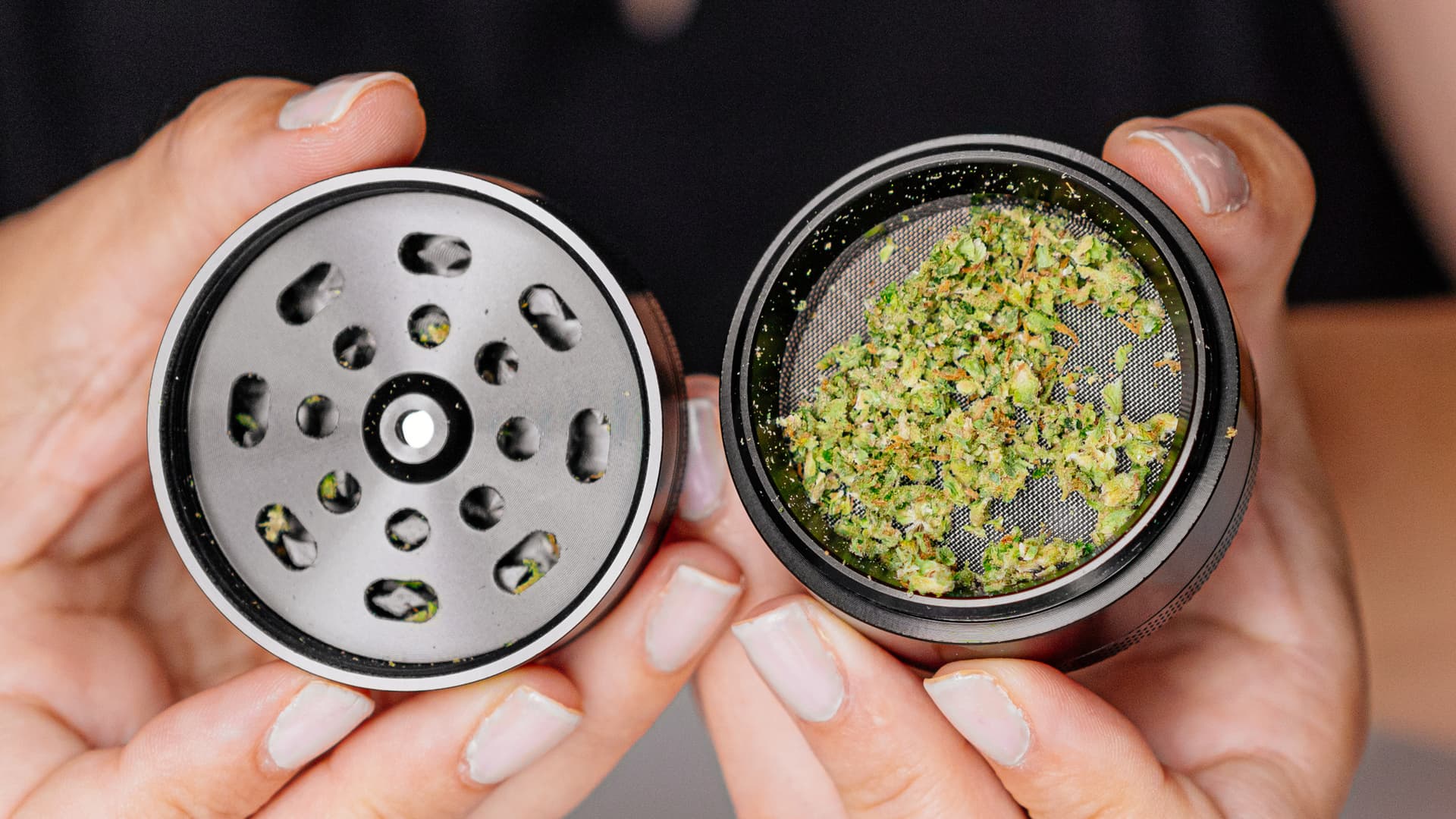 A pile of freshly ground cannabis next to an open grinder on a wooden cutting board, natural light from the side