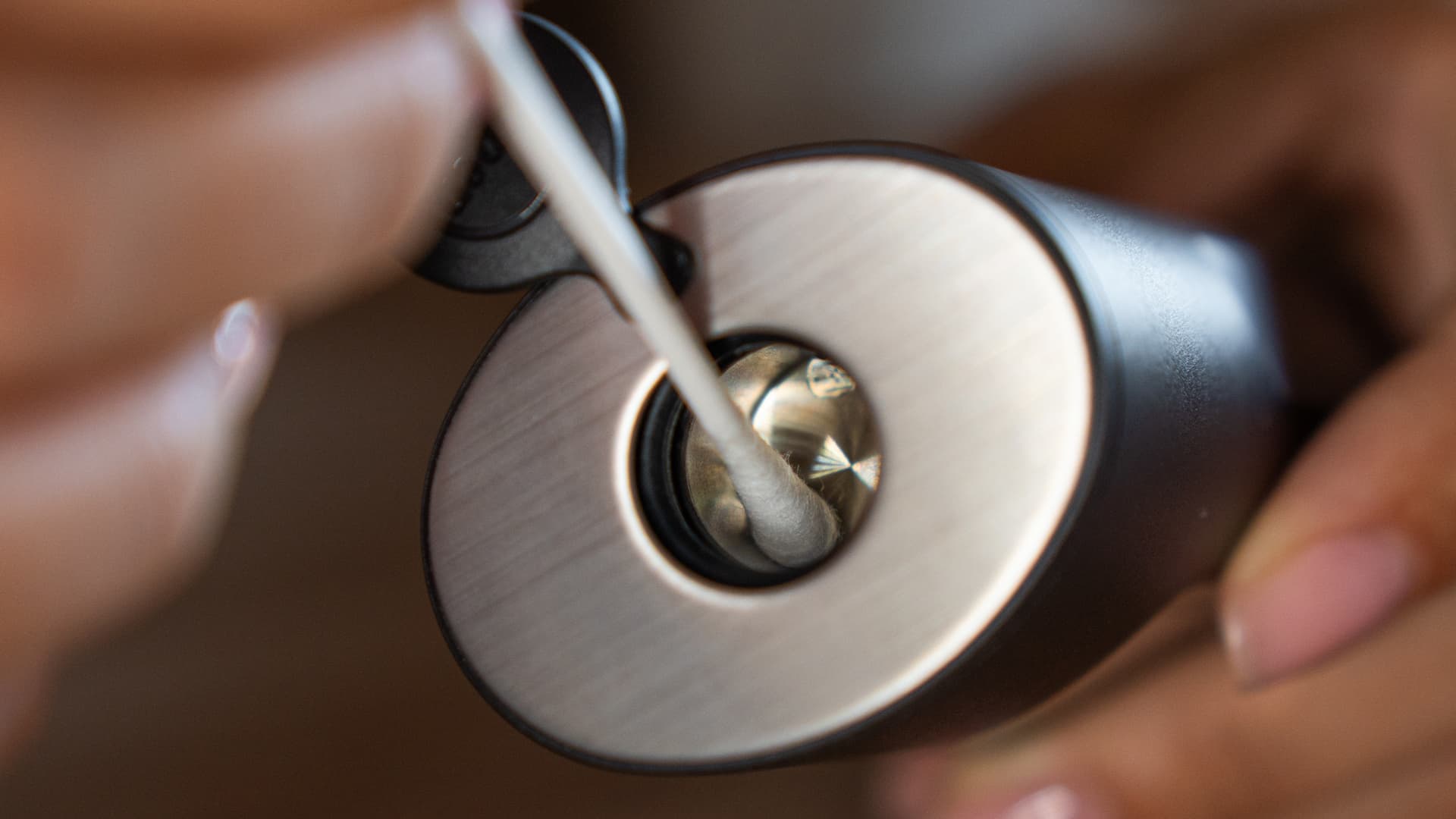 Hands swabbing inside an exposed ceramic vaporizer oven with an alcohol-dipped cotton swab