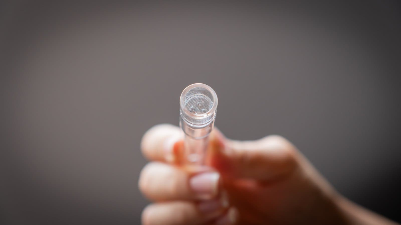 Hand hält Glasröhrchen, Spitze mit Mesh-Sieb im Fokus