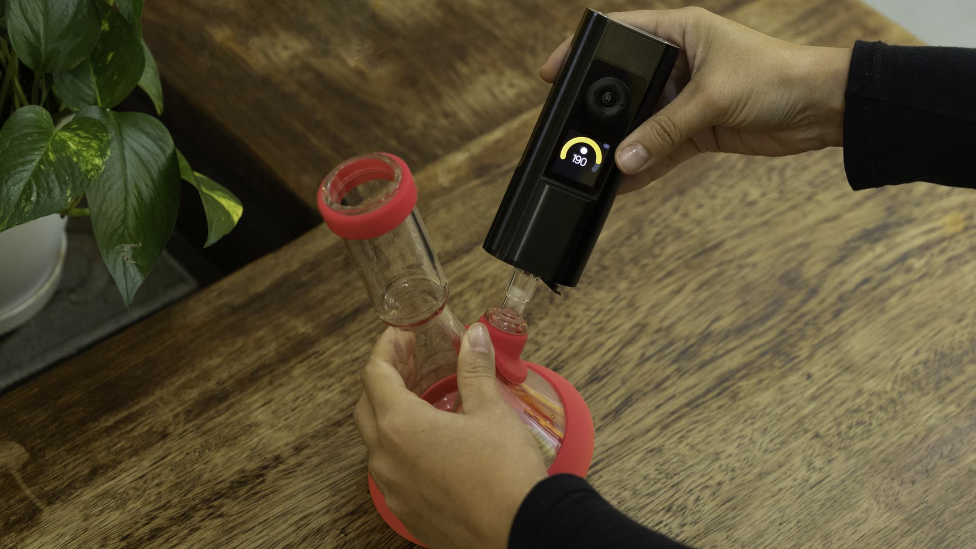 Hands connecting an Arizer Solo 3 to a small glass bong from above, temperature display reading 190°C as the vape seats into the water pipe adapter