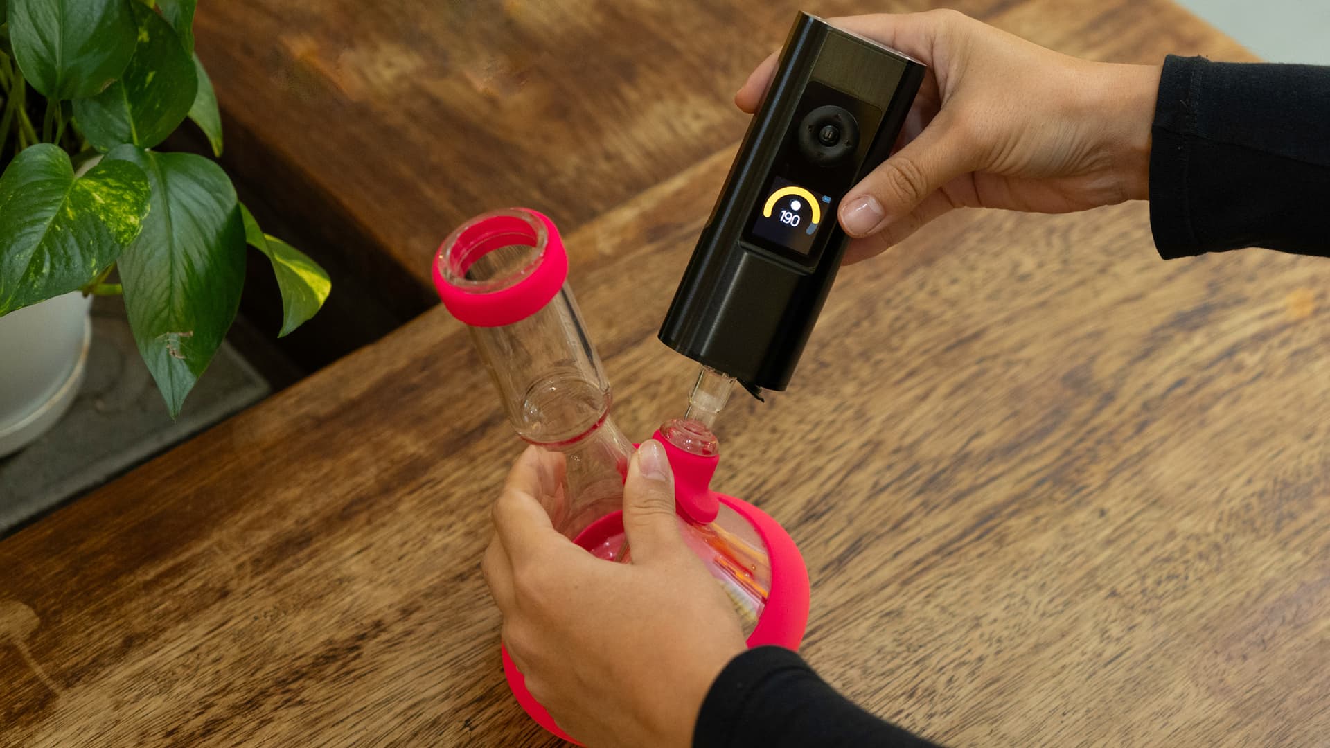 A portable vaporizer connected to a small glass bubbler via a 14mm water pipe adapter on a wooden table.