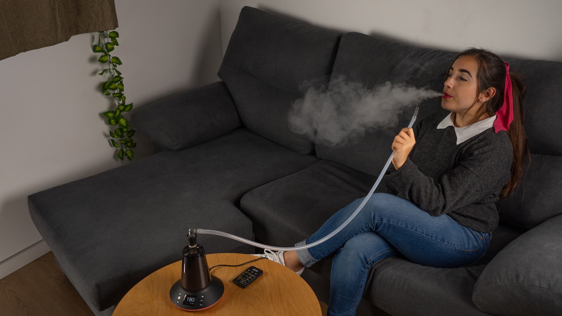Woman using Arizer XQ2 in whip mode on sofa, exhaling vapor with remote control nearby