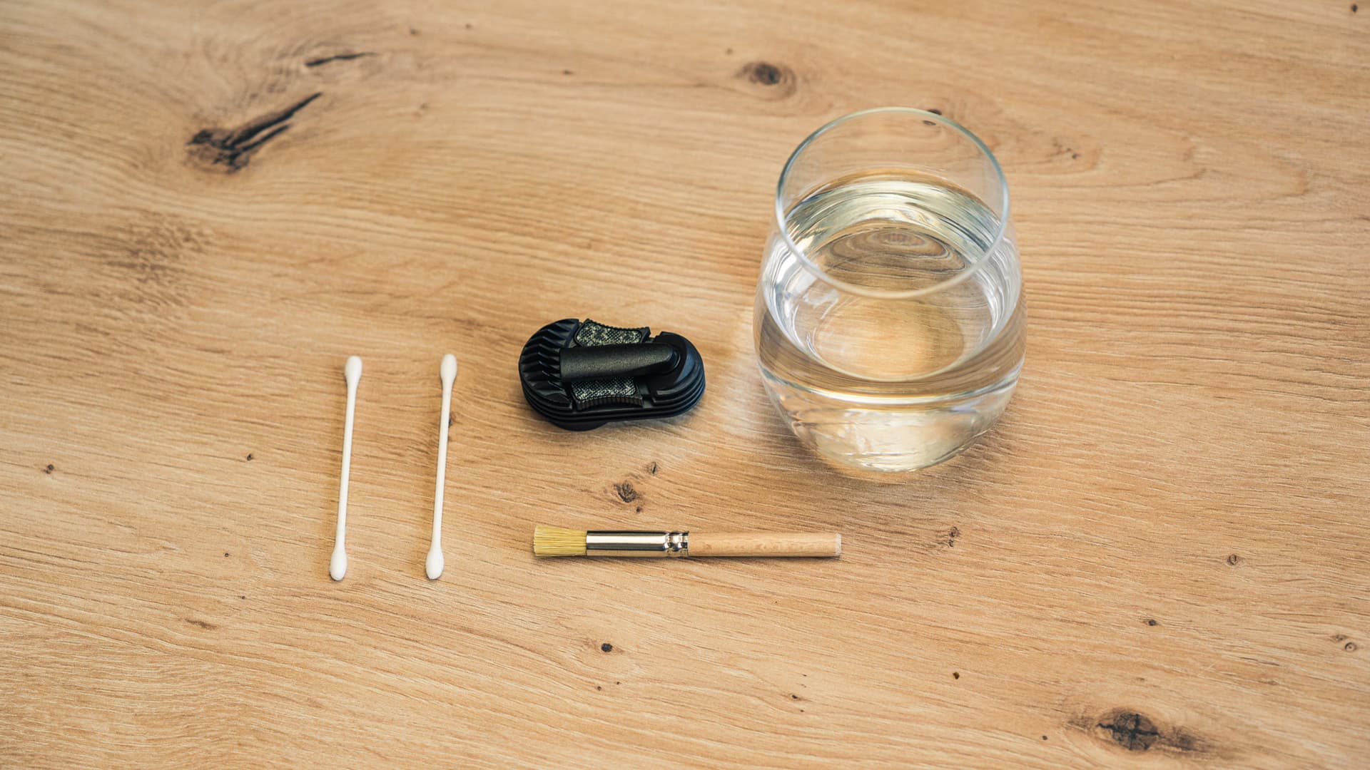 Flat-lay of vaporizer cleaning supplies on a wood surface: isopropyl alcohol, cotton swabs, brush, and a Crafty+ cooling unit