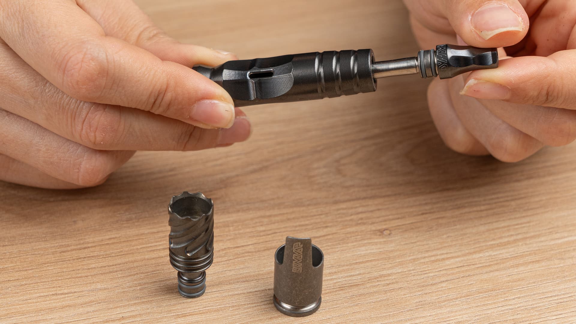 Hände zerlegen den DynaVap HyperDyn, HyperStem, Hyper Tip und Hyper Cap liegen getrennt auf Holzfläche