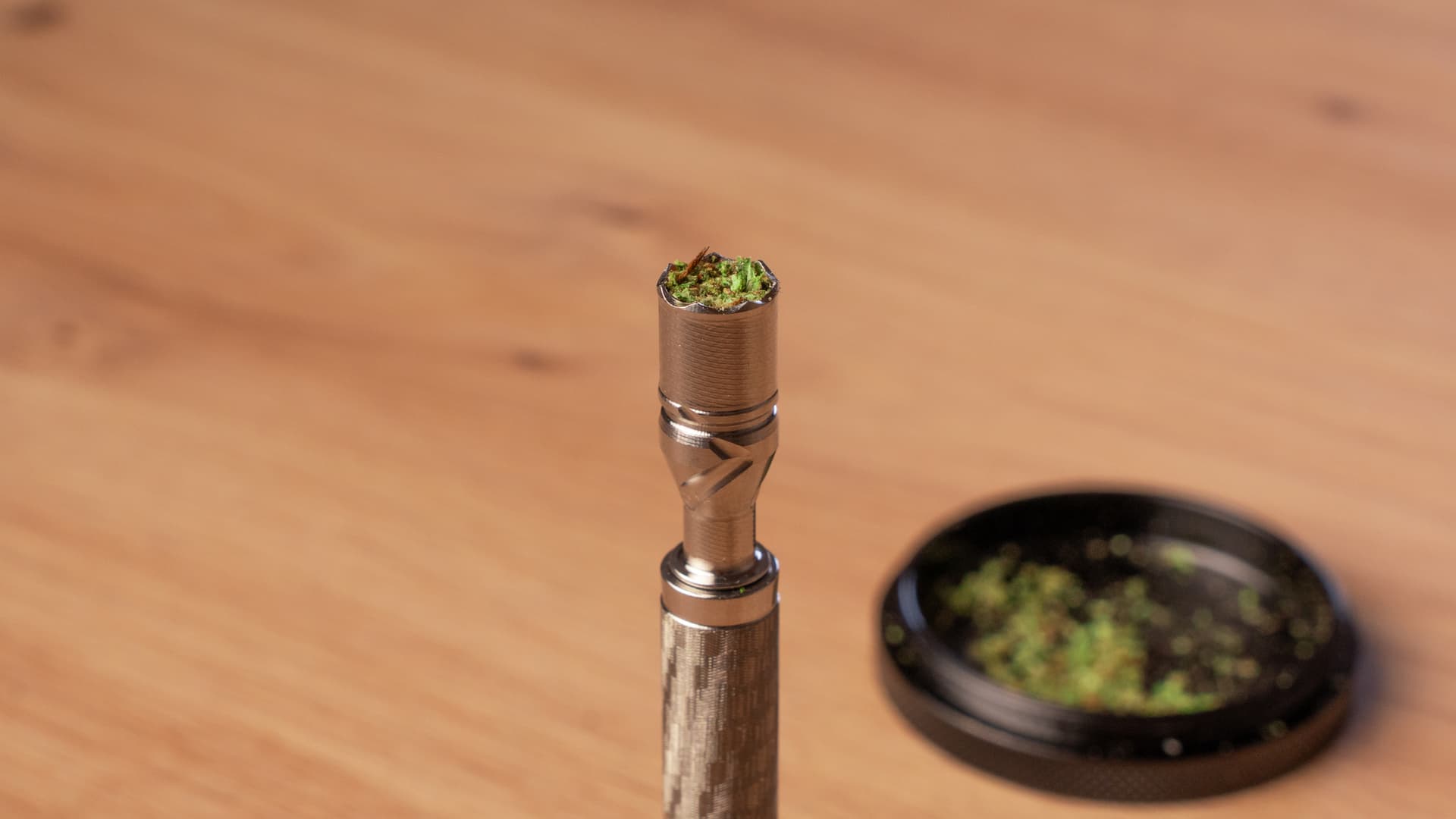 A small DynaVap chamber loaded with finely ground cannabis filling the oven completely, photographed from above on a wood surface
