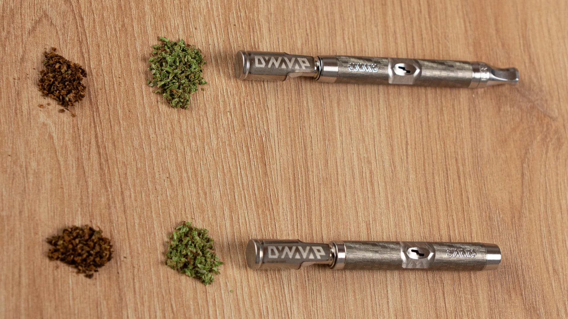 Two DynaVap M7 units lying on a wooden surface with small piles of ground herb at different grind consistencies beside each device