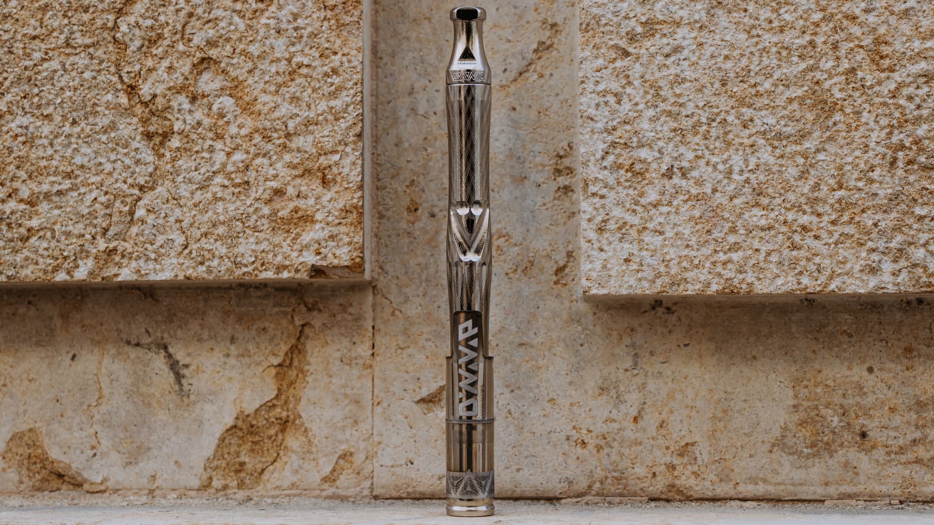 A pen-style conduction vaporizer held vertically against a warm wood surface