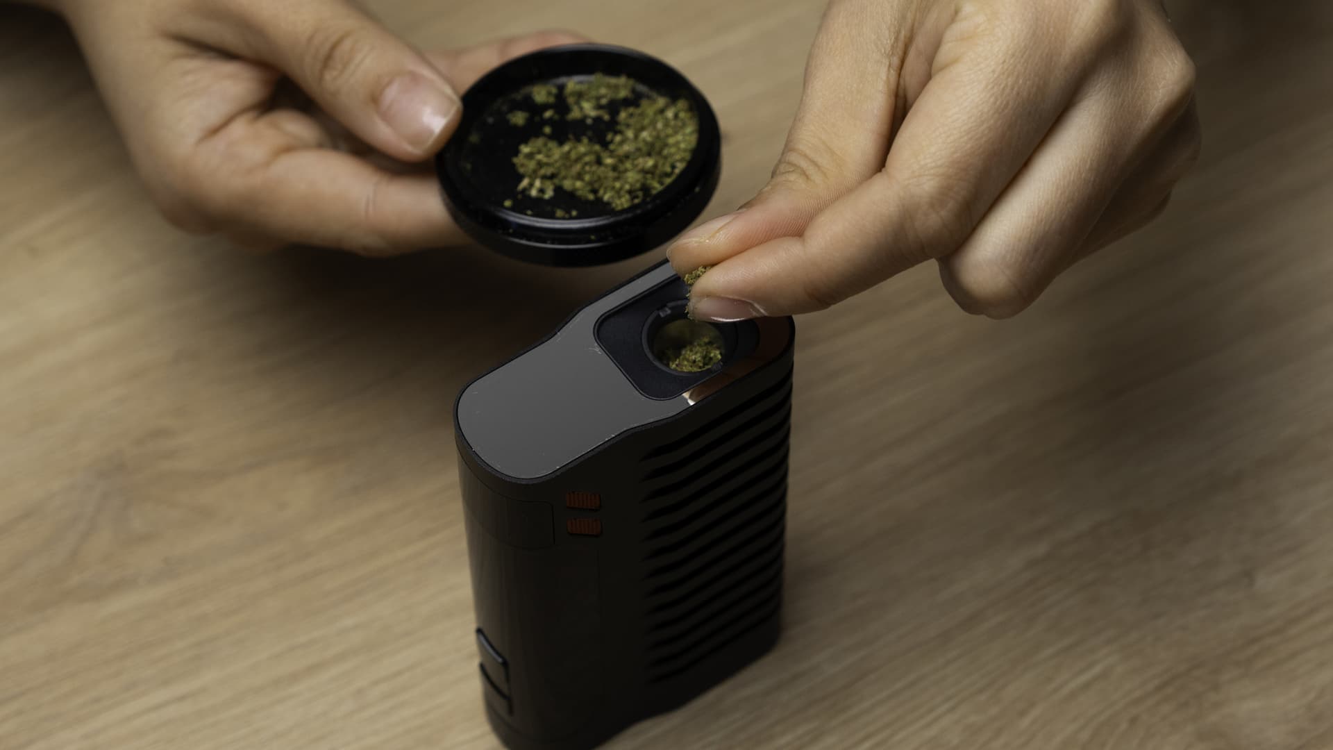 Fenix 2 MAX titanium oven being loaded with ground cannabis from a grinder on a wooden surface