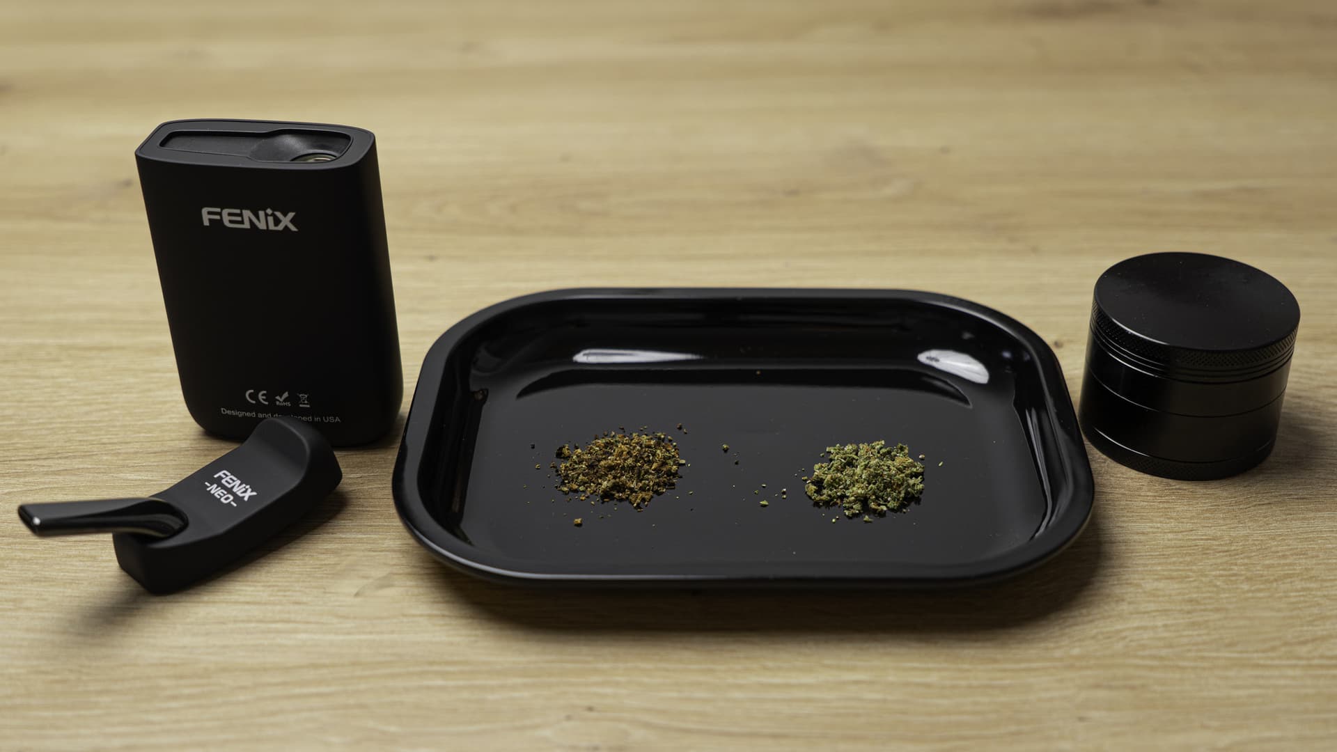 Side-by-side comparison of fresh green ground cannabis and dark brown already-vaped bud on a black rolling tray next to a Fenix NEO vaporizer and herb grinder