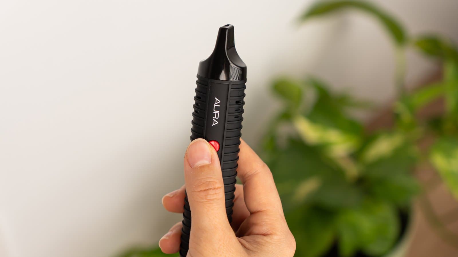 Hand hält den Flowermate Aura aufrecht, Daumen auf der roten Power-Taste