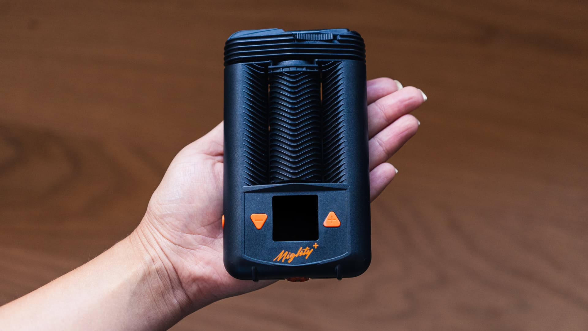 A Mighty+ held in hand showing the OLED temperature display and signature cooling fins along the body