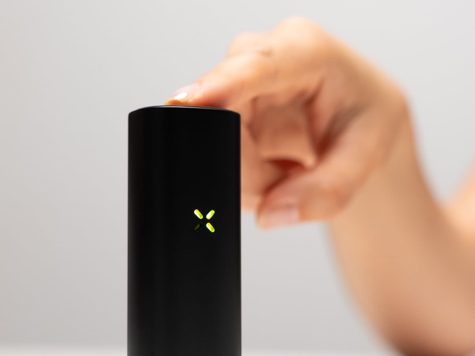 Finger drückt die Mundstücktaste des PAX Flow, die Blütenblätter leuchten grün
