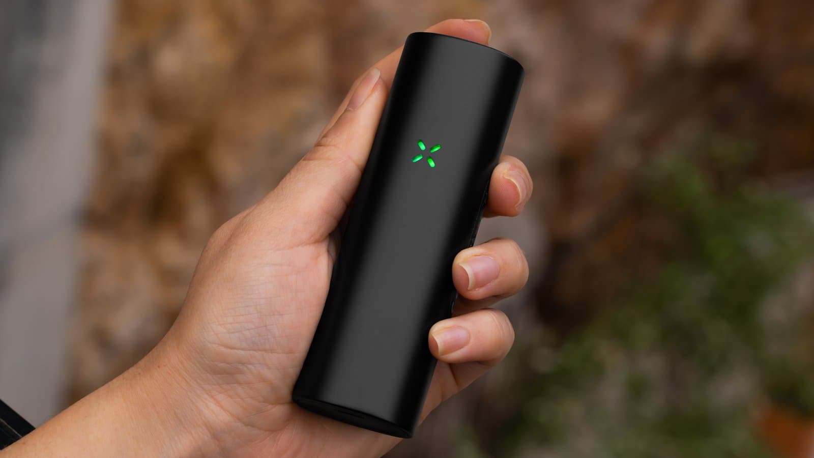 Hand holding the PAX Flow with its petals lit green