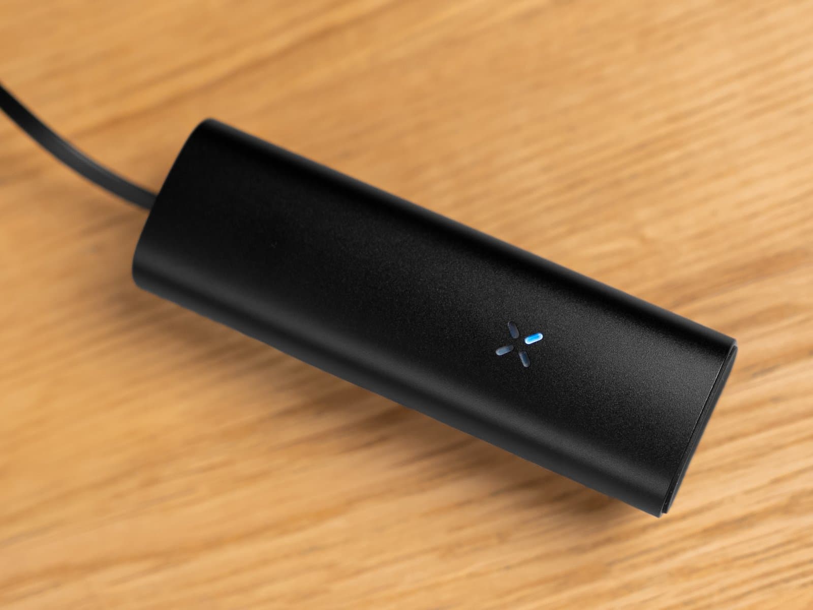Schwarzer PAX Mini 2 lädt auf Holz, blaues LED-Blütenblatt leuchtet