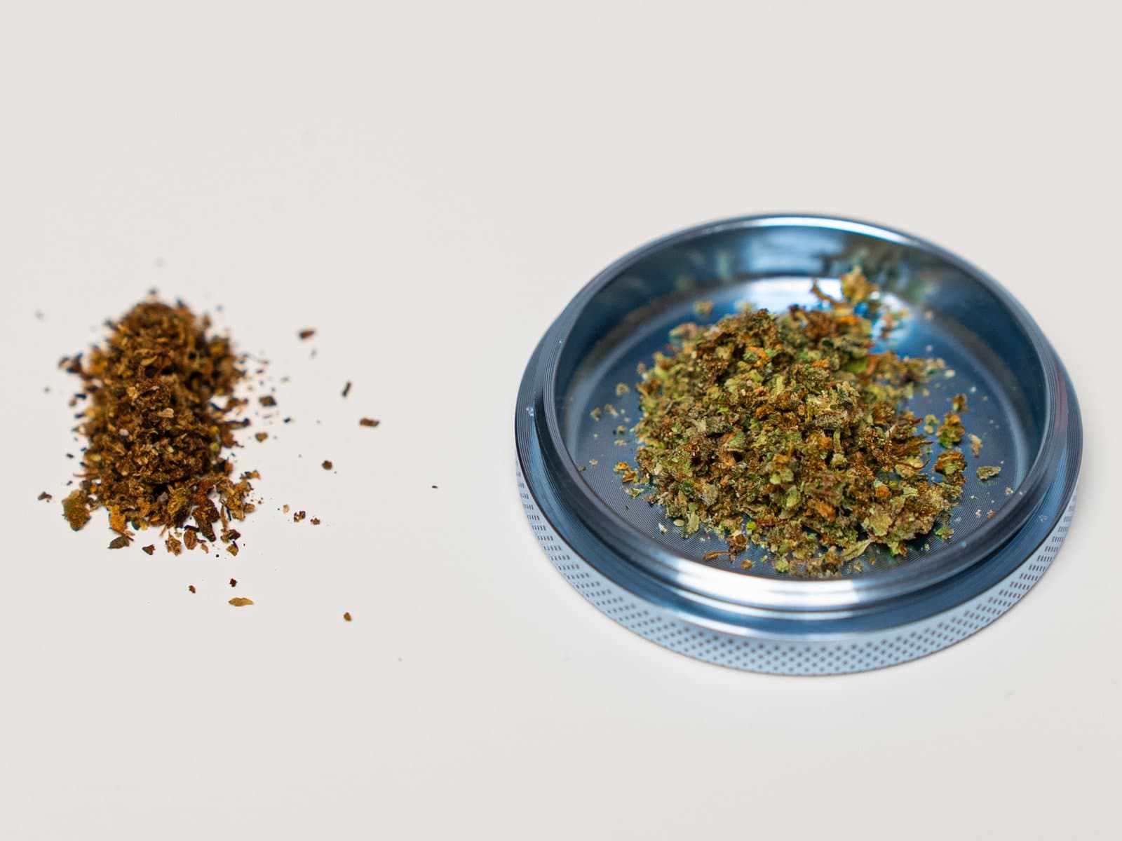 Gebräunter AVB-Haufen neben frischem grünem gemahlenem Cannabis im Grinder