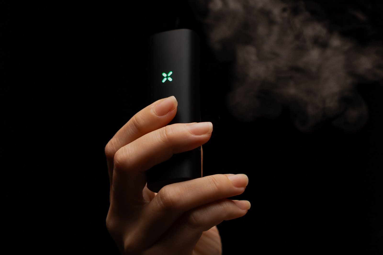 Hand hält PAX Mini 2, grüne LED leuchtet, Dampfwolke zieht vorbei