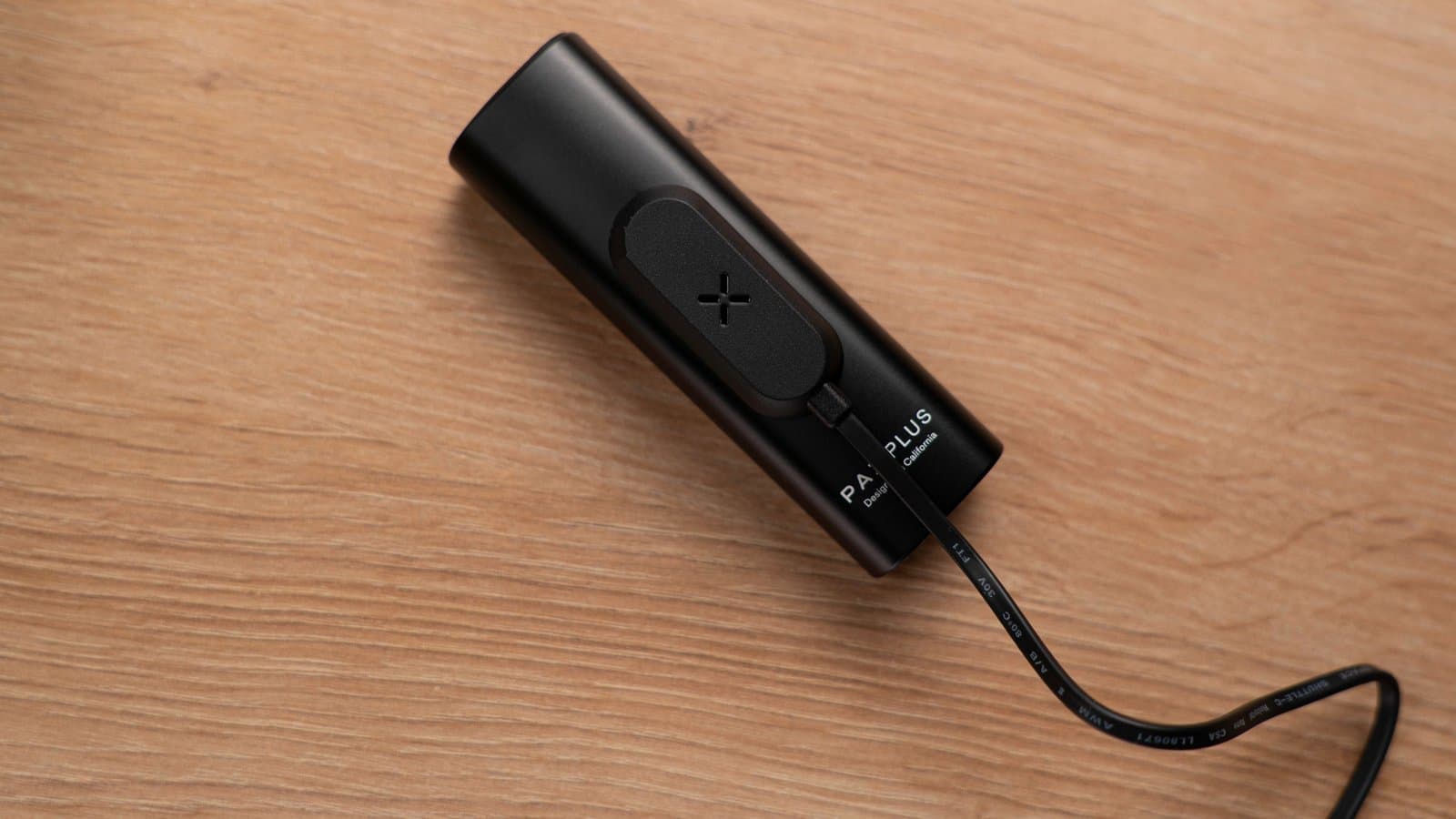 Schwarzer PAX Plus auf Holz, verbunden mit dem magnetischen USB-Ladepuck