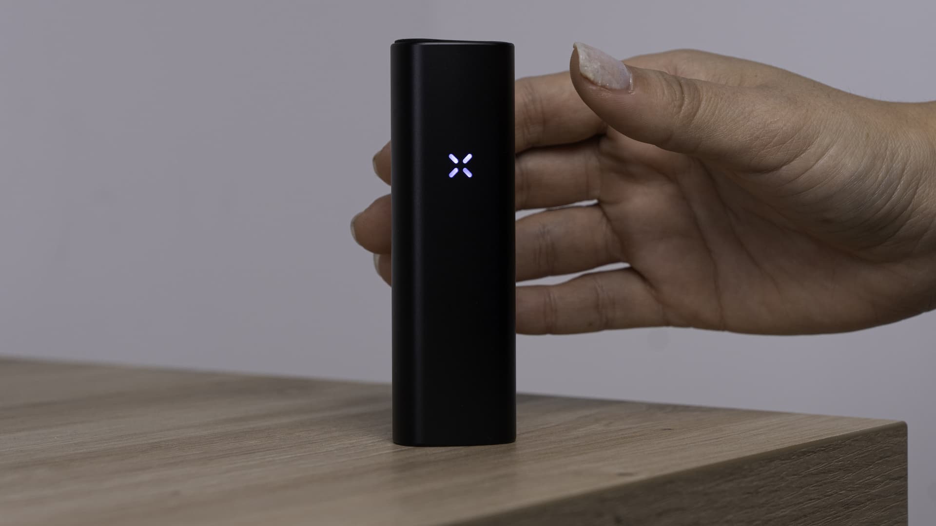 Hand nimmt den PAX Plus hoch, während die lila Blüten-LEDs leuchten und der Bewegungssensor ihn aufweckt