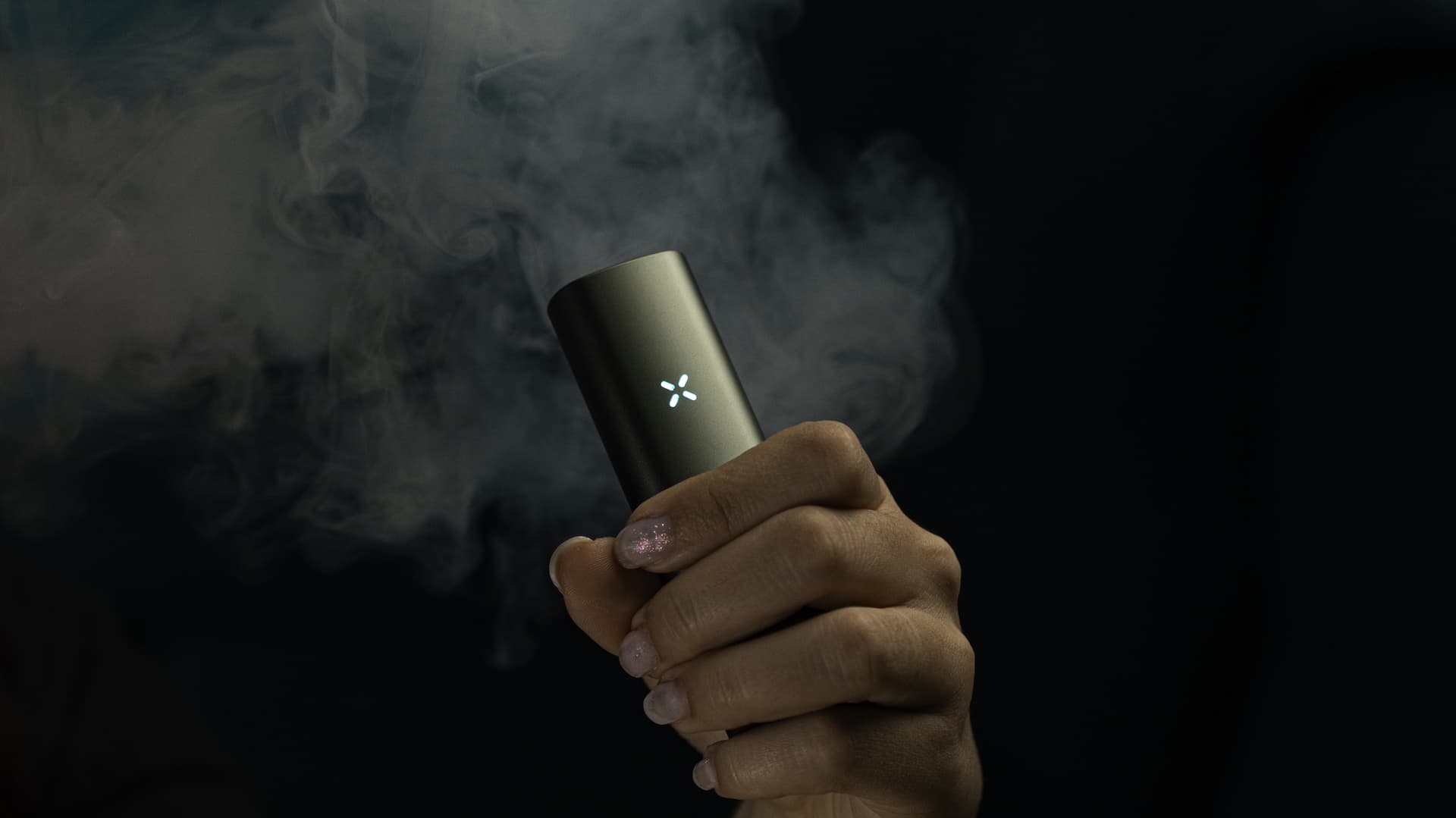 PAX Plus erzeugt eine sichtbare Dampfwolke, in der Hand gehalten vor dunklem Hintergrund