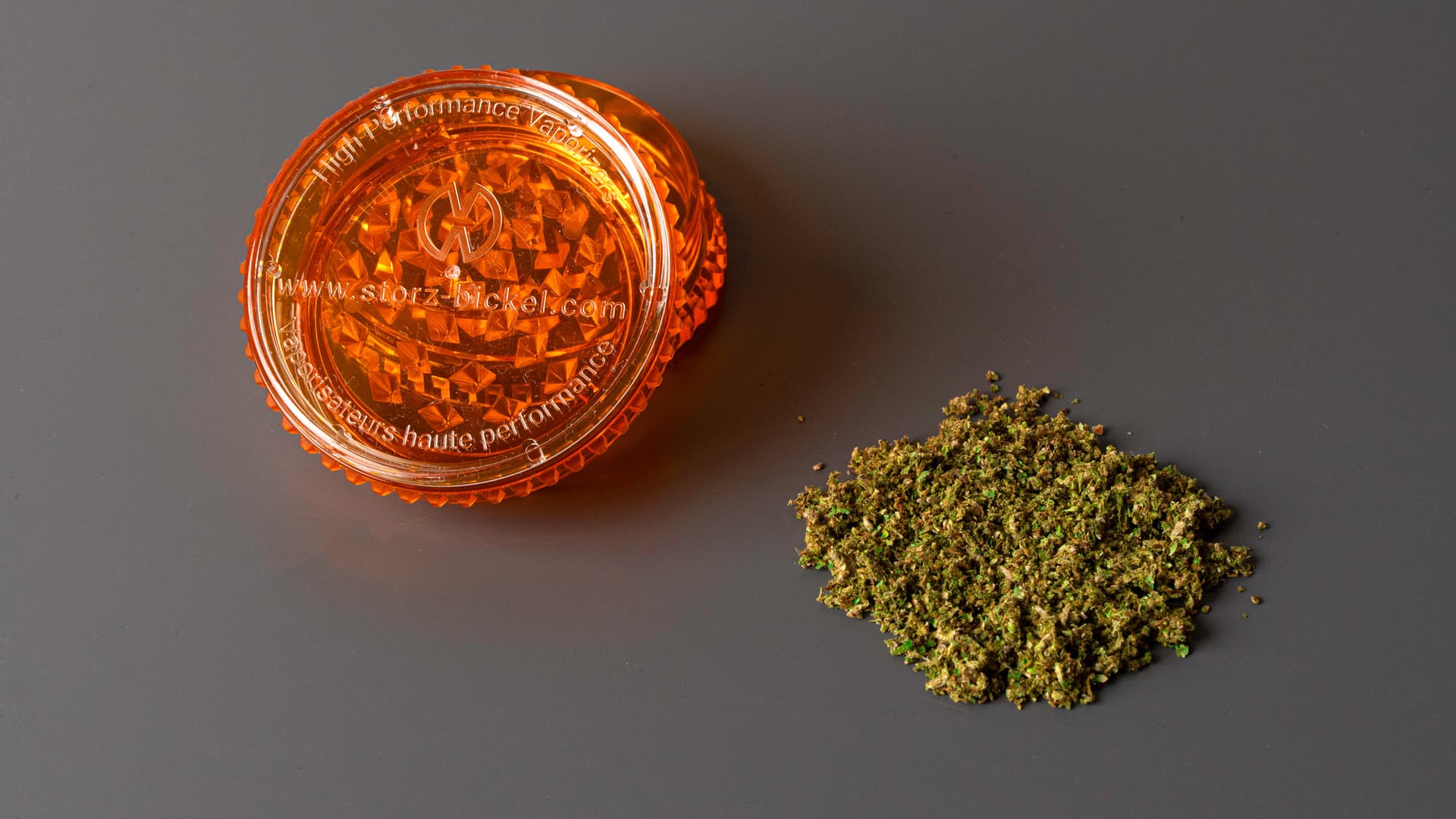 Orange Storz & Bickel grinder next to a pile of ground cannabis