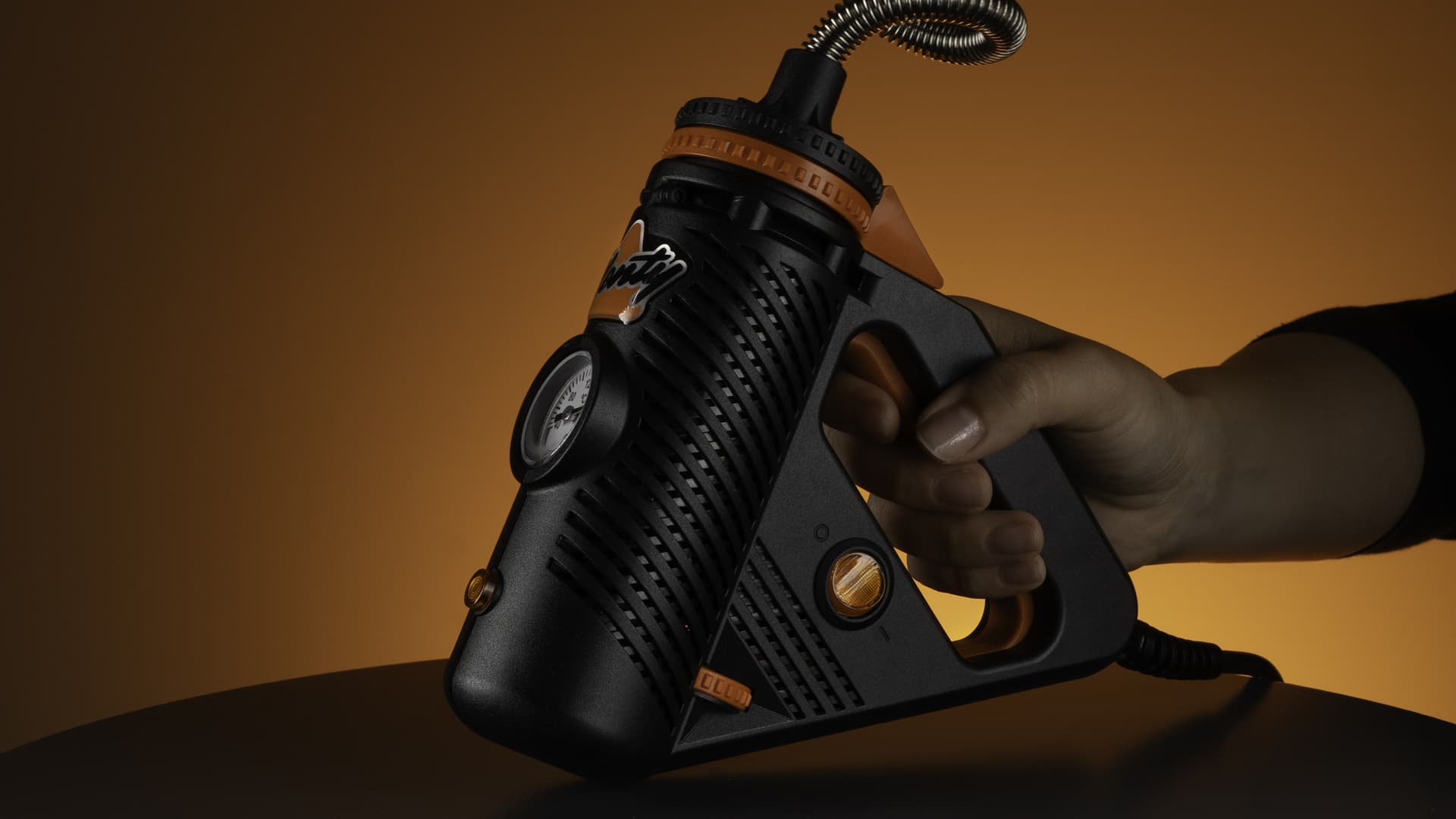 The Plenty vaporizer held in a hand with its distinctive stainless steel cooling coil visible against a warm wooden surface