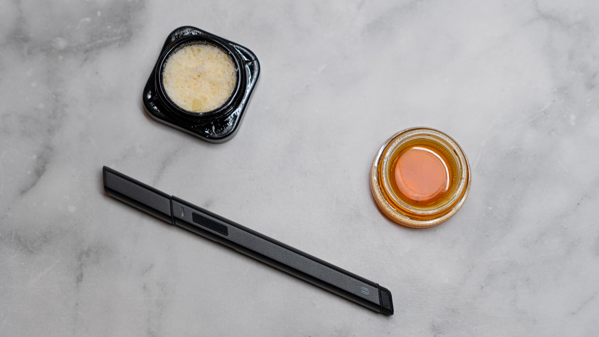 Puffco Hot Knife heated loading tool on marble surface alongside two open glass concentrate jars, one with crumble sugar wax and one with golden live resin sauce