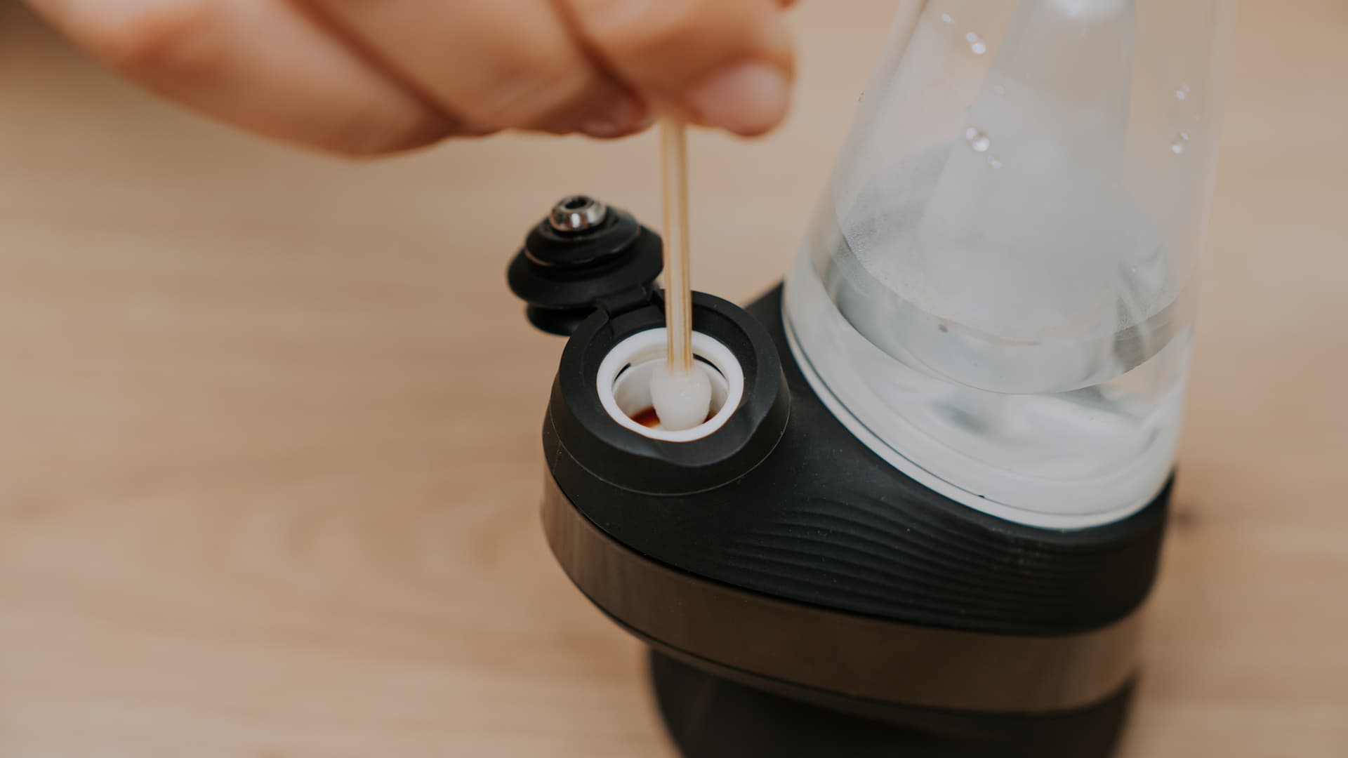 A cotton swab being used inside the heating chamber of an eRig to wipe residue from the inner walls