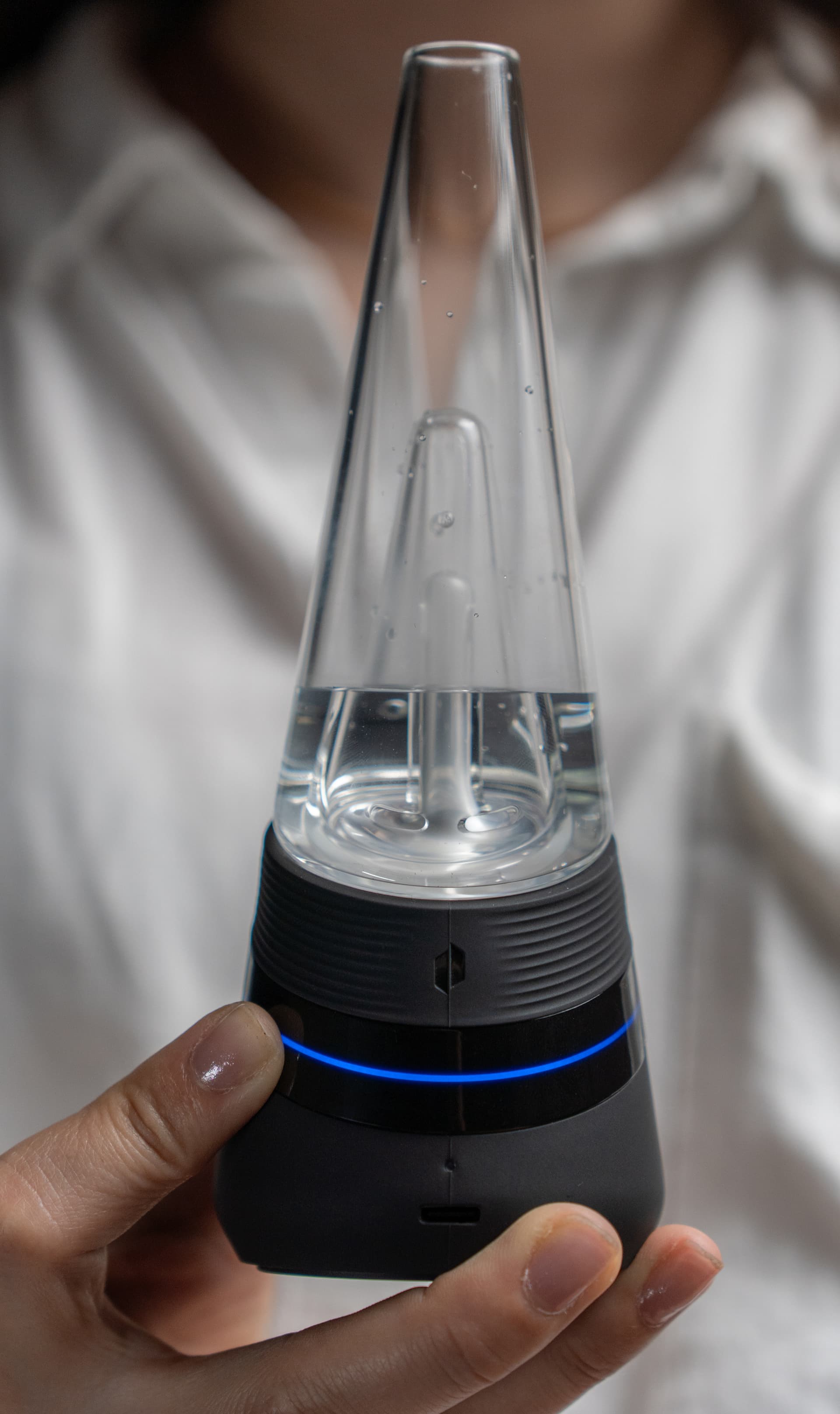 Hand hält den Puffco New Peak mit blau leuchtendem LED-Ring im niedrigen Preset, Daumen auf dem Knopf