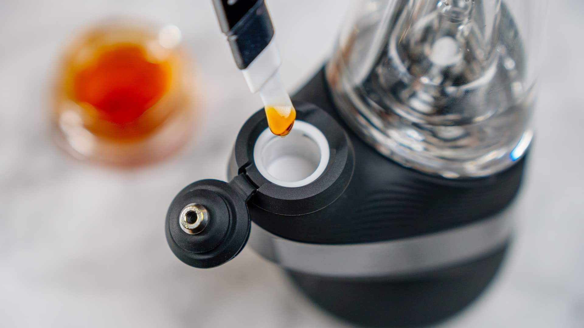 A small dab tool placing a golden bead of concentrate into the ceramic chamber of an electronic dab rig, warm tones and shallow depth of field.