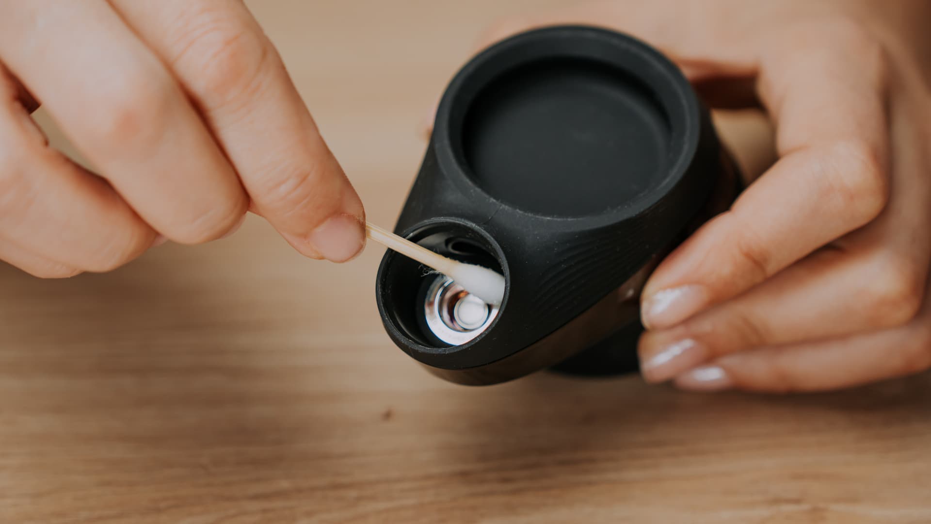 A hand using a cotton swab to clean the Puffco Peak ceramic chamber atomizer