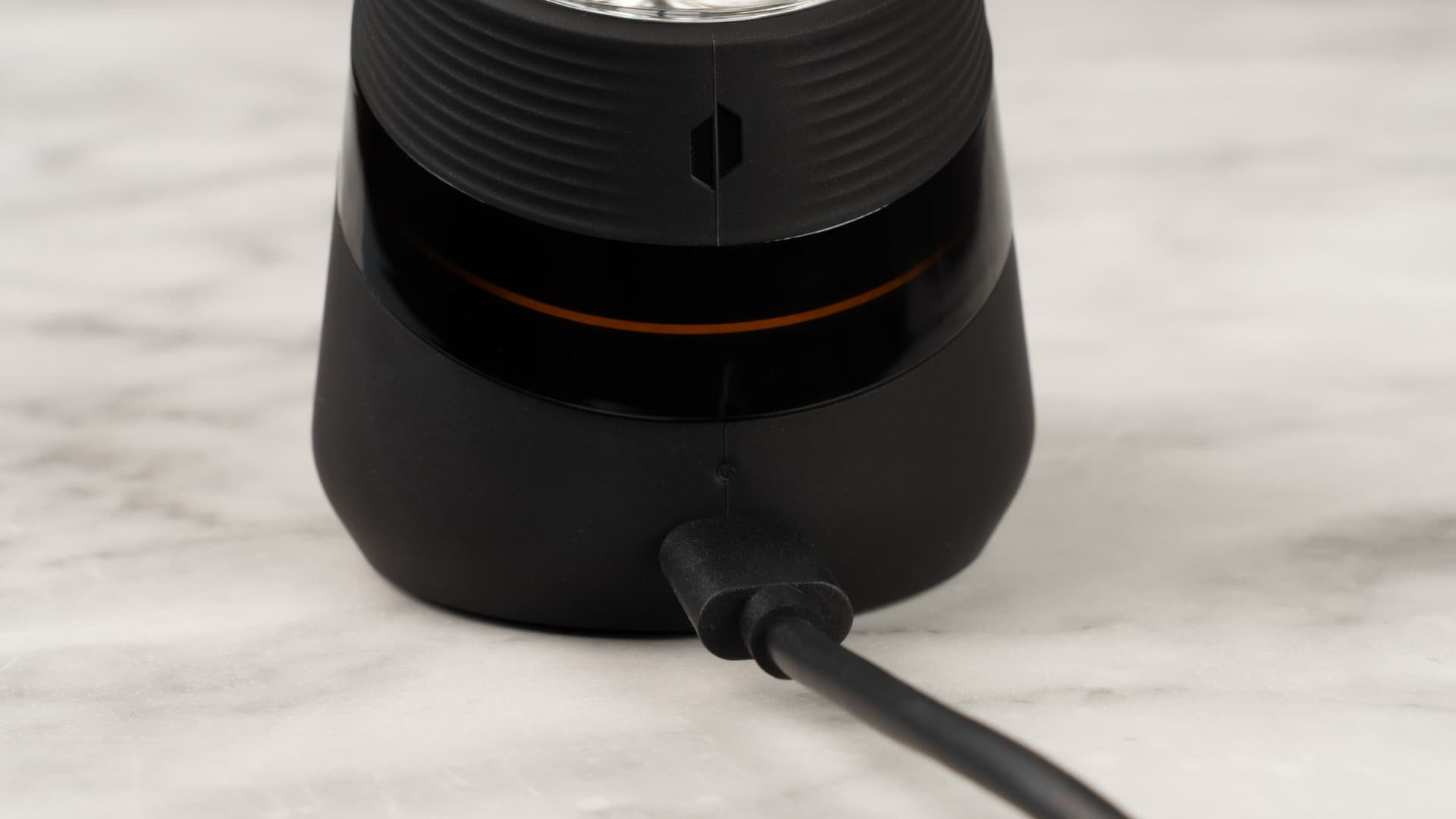 Basis des Puffco New Peak am USB-C-Kabel angeschlossen, orange leuchtende LED zeigt den Ladevorgang an