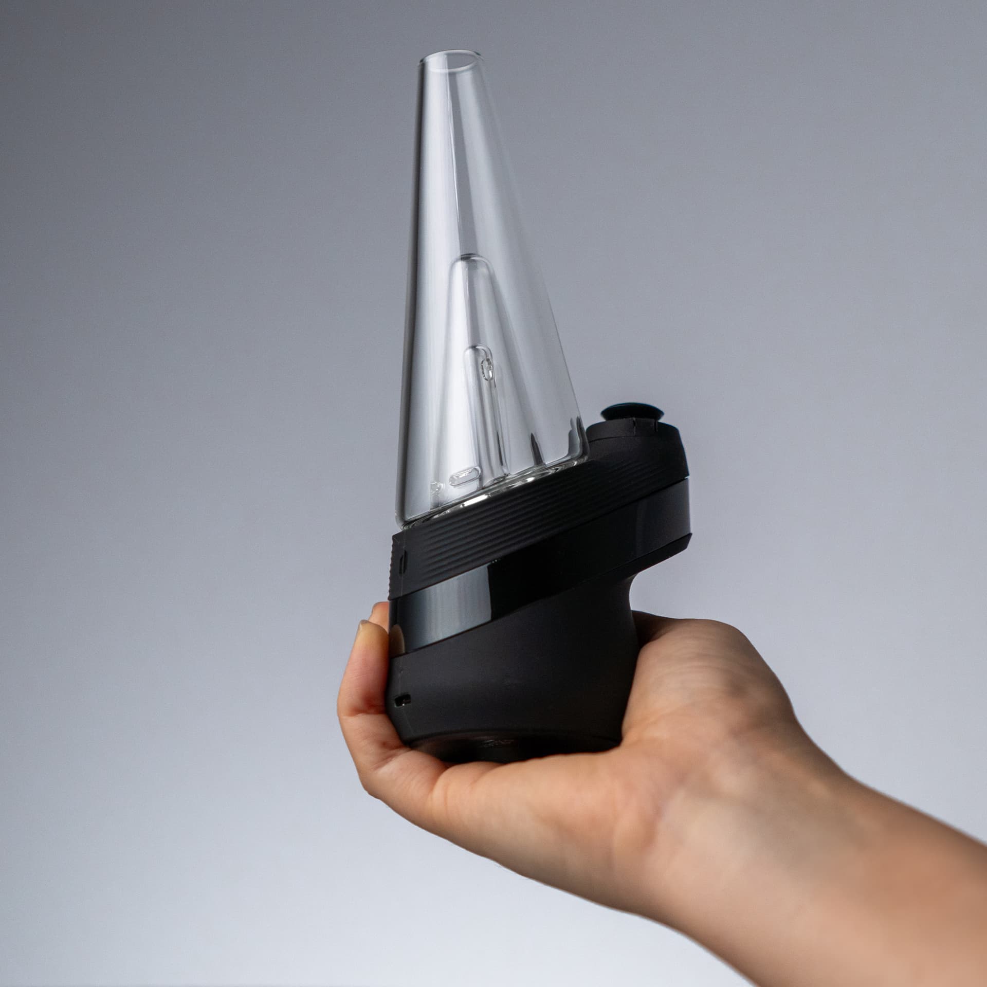Hand hält den Puffco New Peak und zeigt die kompakte Einhand-Größe mit aufgesetztem Glas-Bubbler