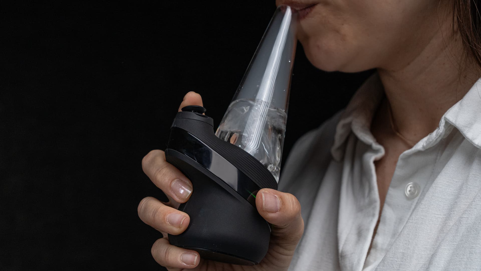 Person zieht am aufrecht gehaltenen Puffco New Peak, Dampf im Glas-Bubbler sichtbar