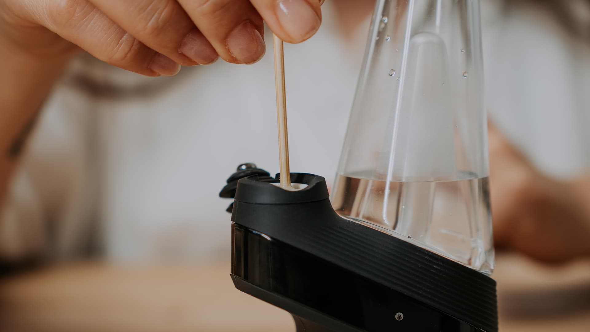Holzstäbchen in der offenen Kammer des Puffco New Peak, Joystick-Cap angehoben und Wasser im Glas