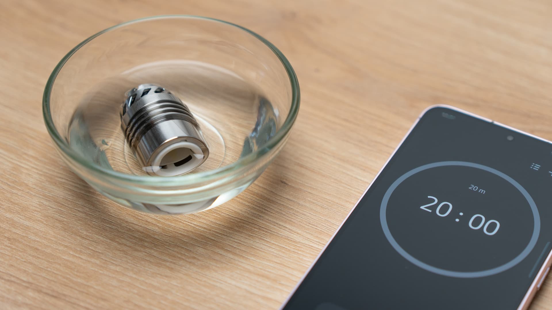 A disassembled eRig atomizer submerged in a small glass bowl of clear isopropyl alcohol