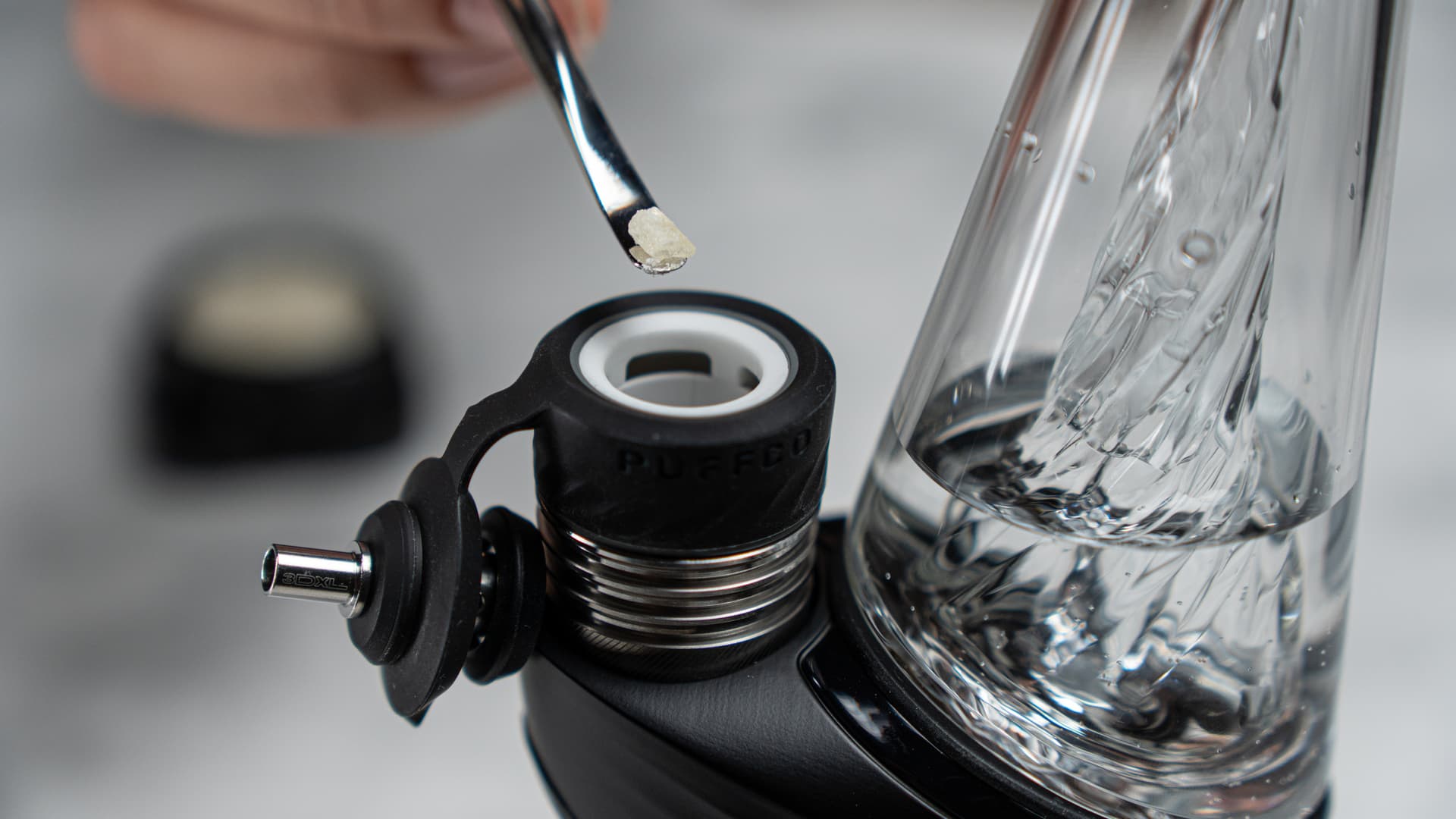 Close-up of a metal dab tool holding a rice-grain sized amount of golden concentrate being lowered into the Puffco Peak Pro 3DXL ceramic 3D Chamber