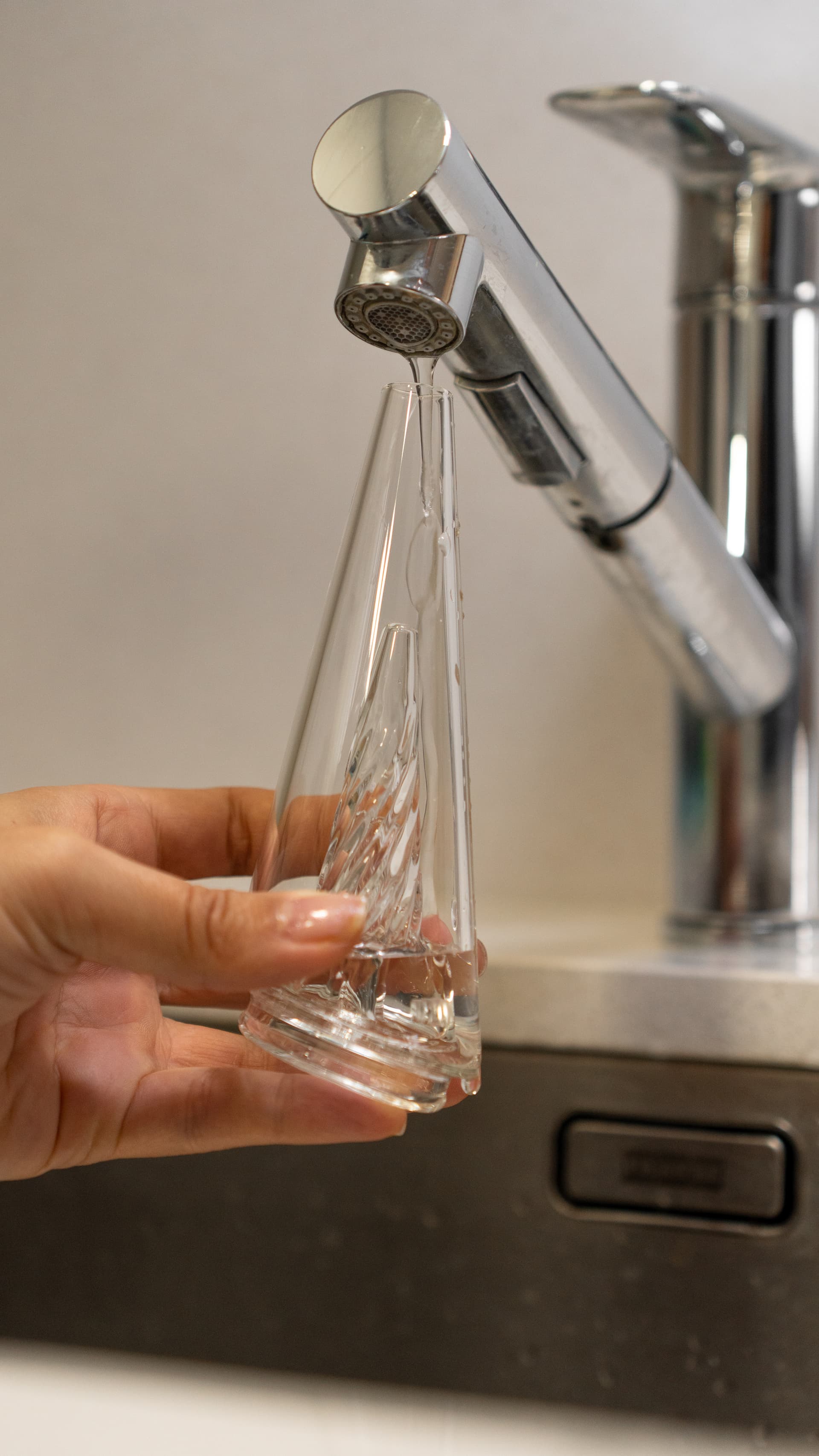 Hands rinsing a glass eRig bubbler under running water in a sink