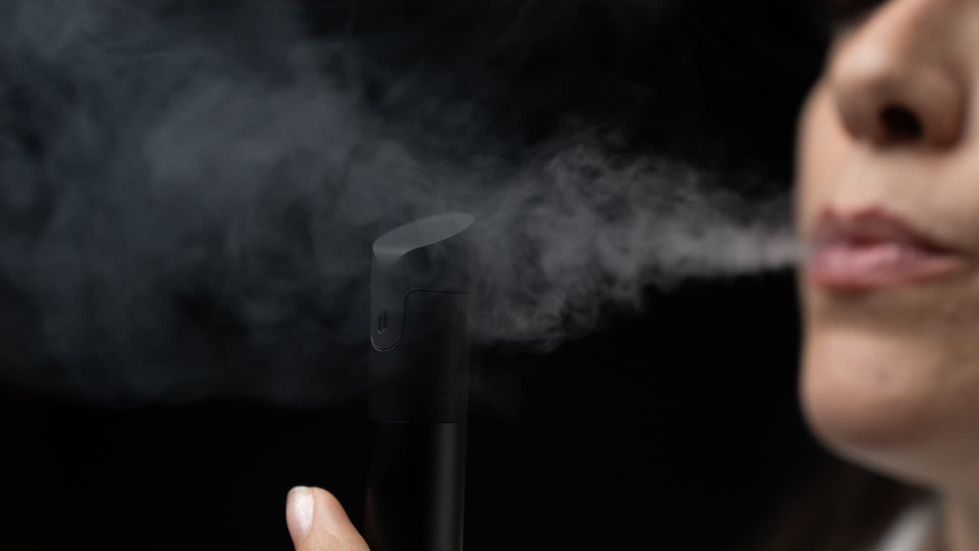 Person atmet Dampf aus dem Puffco Pivot vor dunklem Hintergrund aus