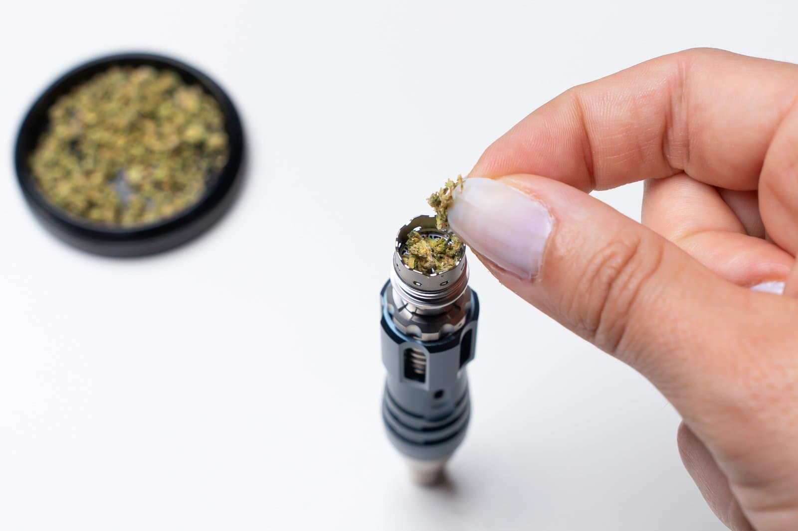 Fingers loading ground cannabis into the Tempest 2 titanium bowl