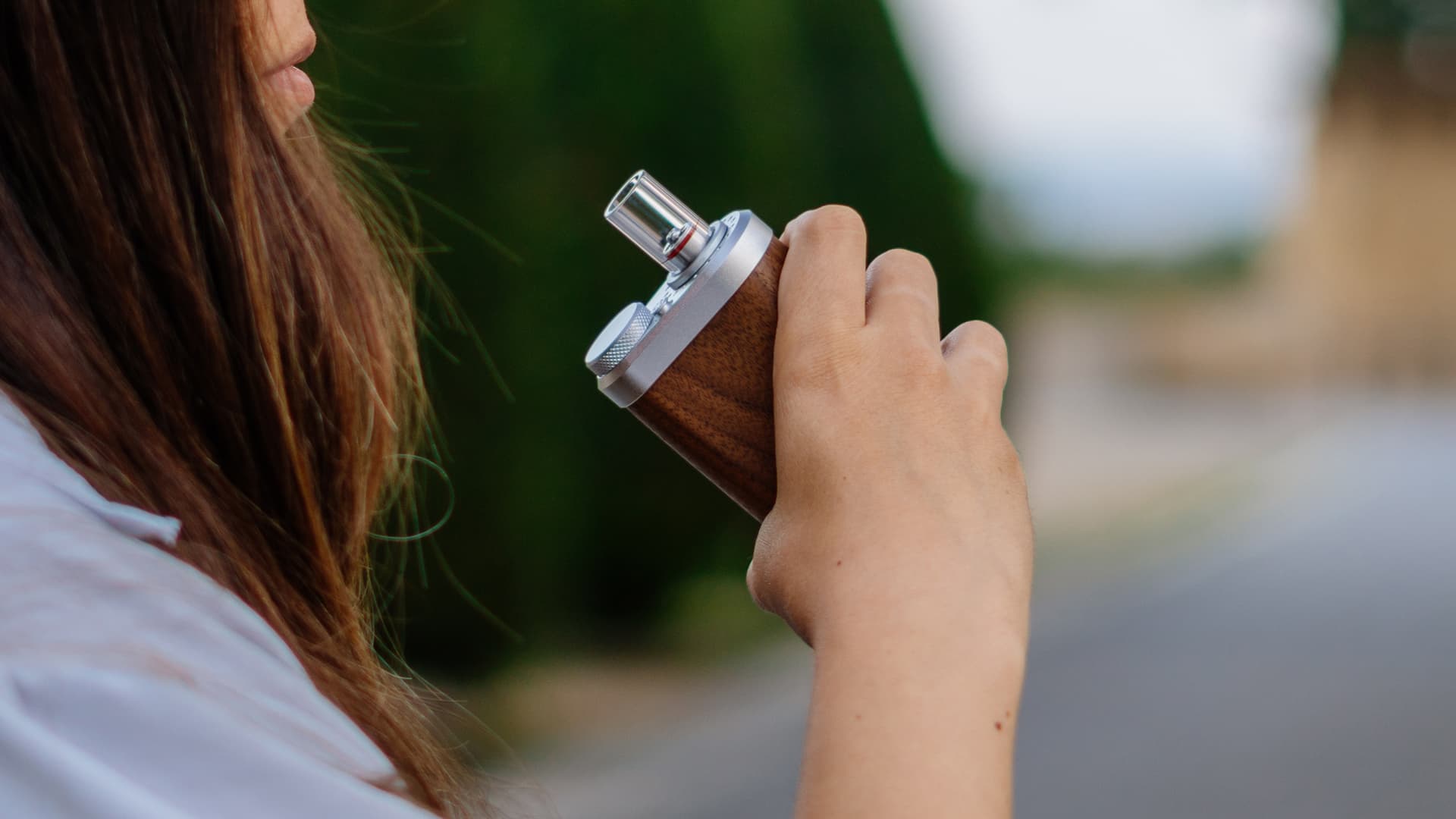 A Tinymight 2 vaporizer held in hand mid-draw with visible vapor production, photographed against a soft natural background