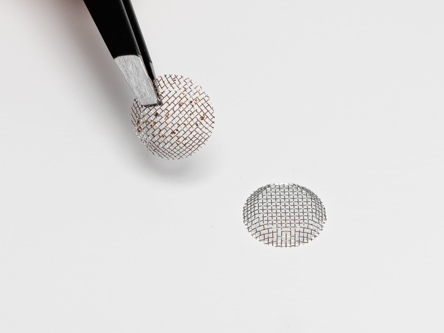 Tweezers holding a used mesh screen above a new one