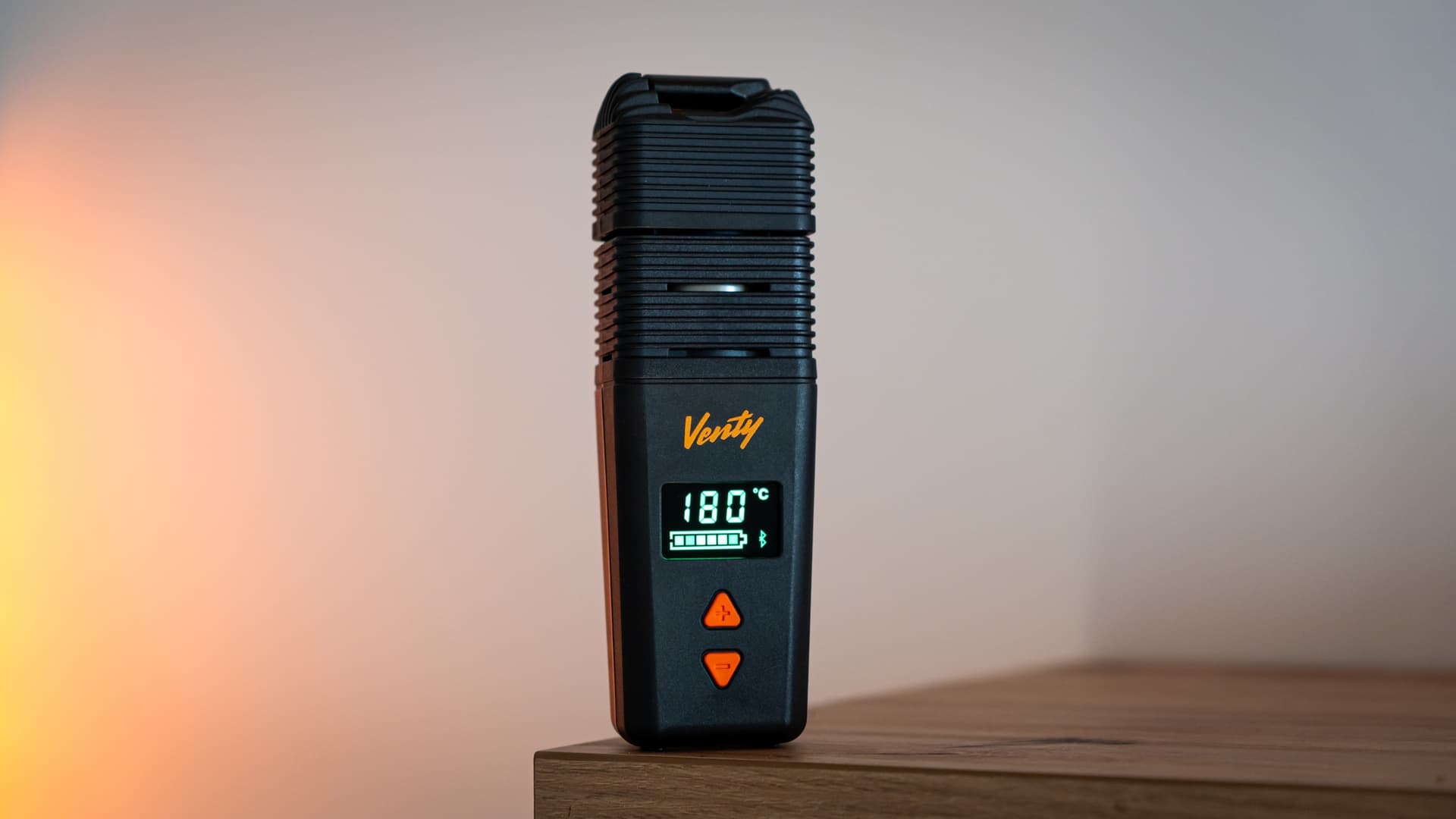 Storz & Bickel Venty vaporizer standing on a wooden table edge with the OLED display showing 180 degrees Celsius and a full battery indicator